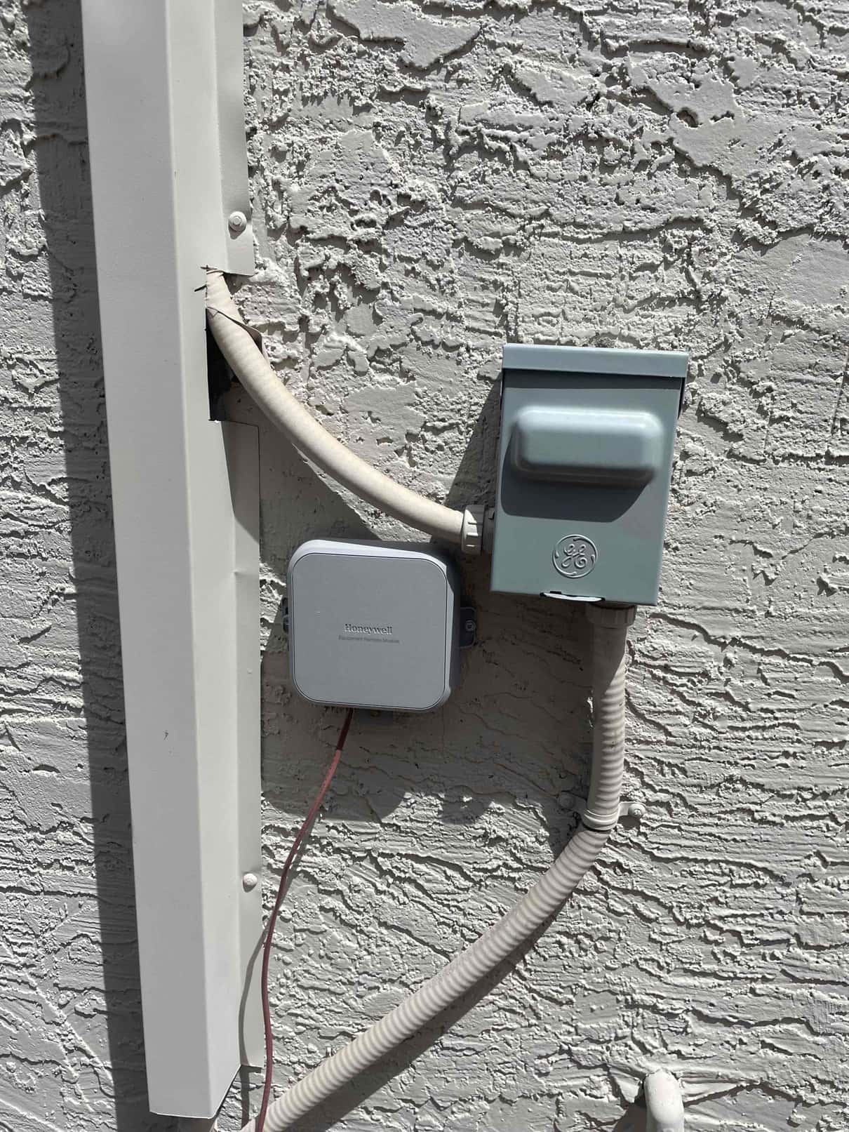 Outdoor AC disconnect with flexible conduit and control box mounted on exterior wall near line-set cover.