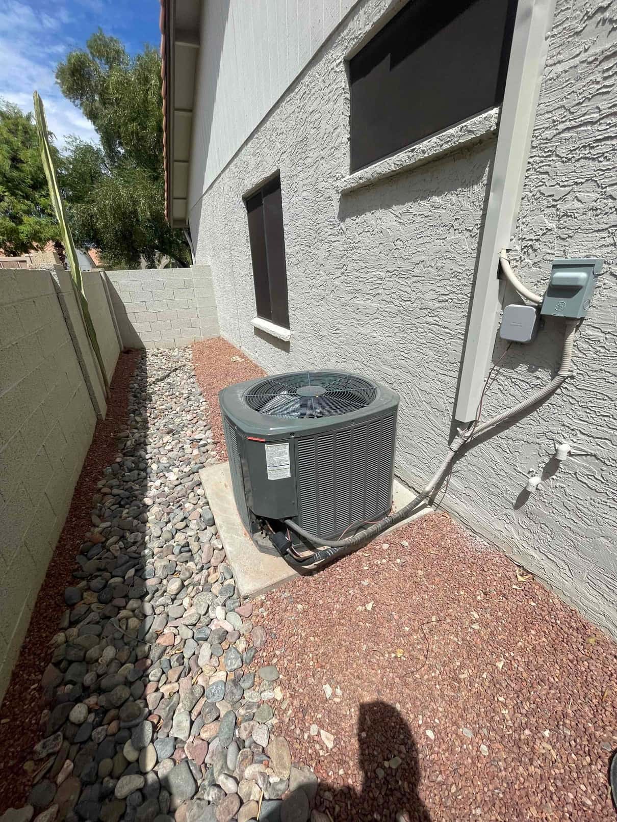 Outdoor air-conditioning condenser on pad with insulated refrigerant lines and wall-mounted disconnect nearby.