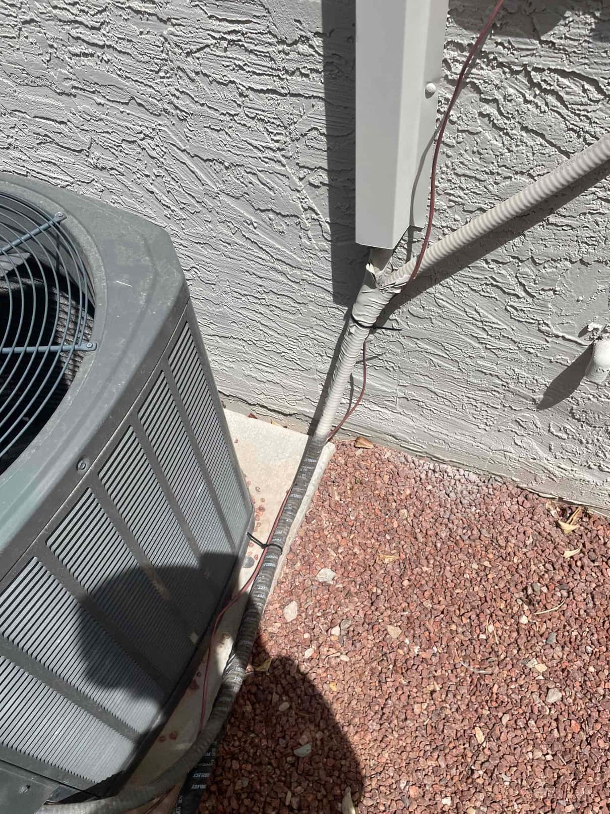 Outdoor condenser beside wall with insulated refrigerant line set and control wires entering a line-set cover.