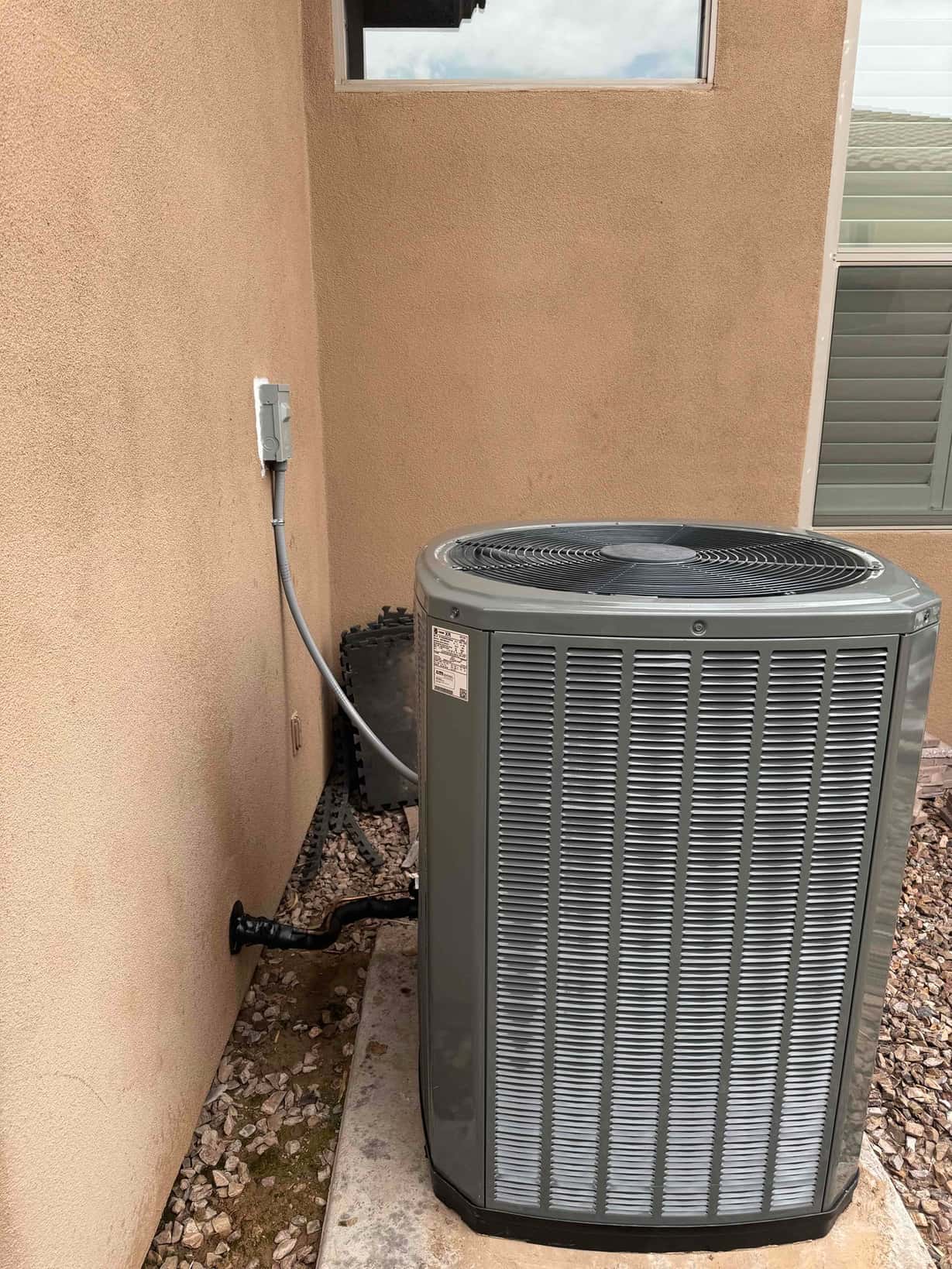 Outdoor condenser set on a level pad with sealed wall penetration and mounted electrical disconnect in place.