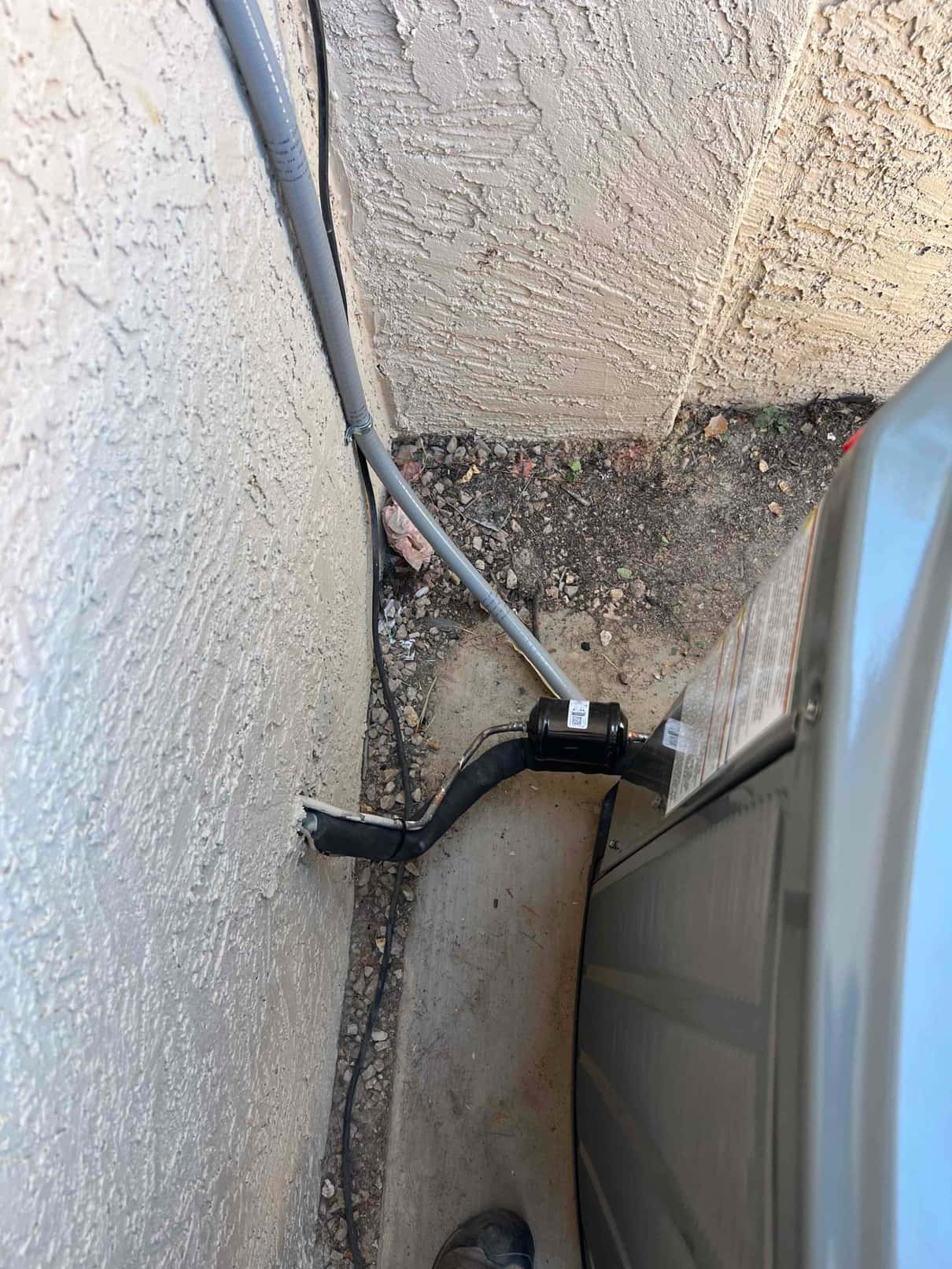 Outdoor condenser set on a pad with insulated refrigerant line set, suction accumulator, and electrical whip routed along the wall.