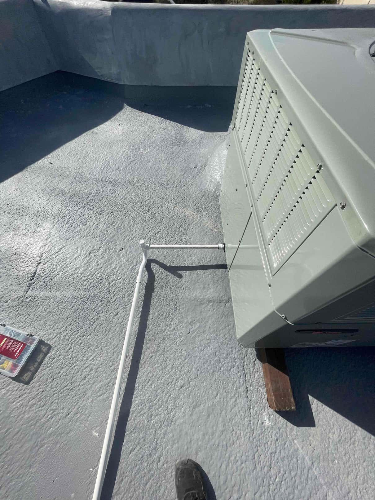 Outdoor condenser set on a rooftop with drain or conduit piping routed alongside and unit elevated on wood supports.