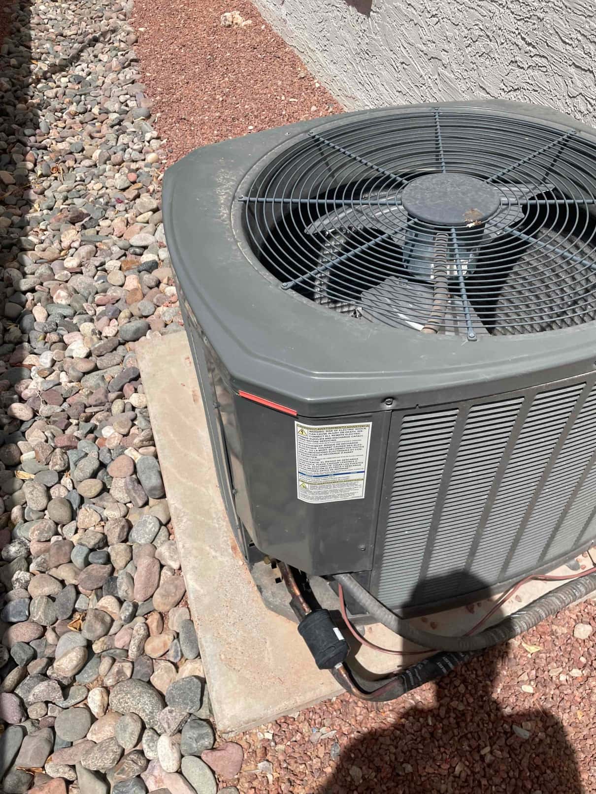 Outdoor condenser unit on pad with top fan grille and insulated refrigerant lines entering the cabinet.