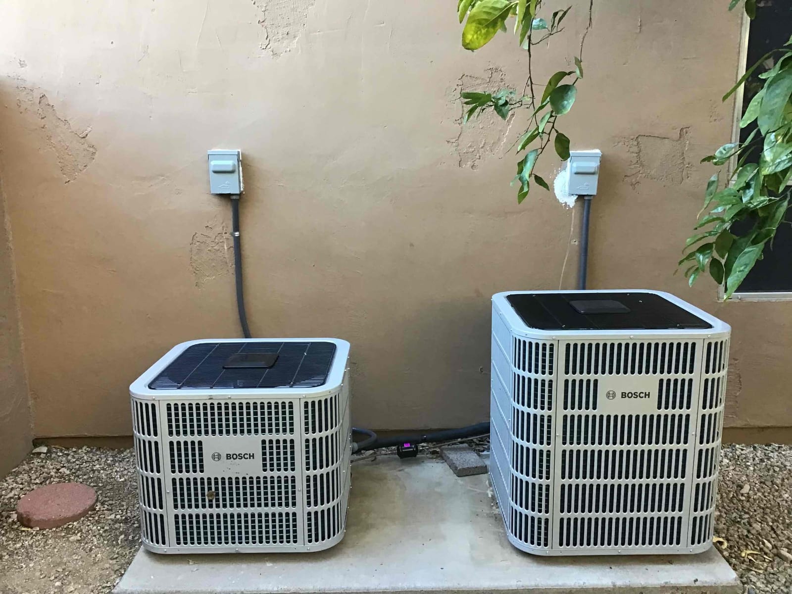 Two outdoor condensers set on pads with weatherproof disconnect boxes and insulated refrigerant lines routed along the wall.