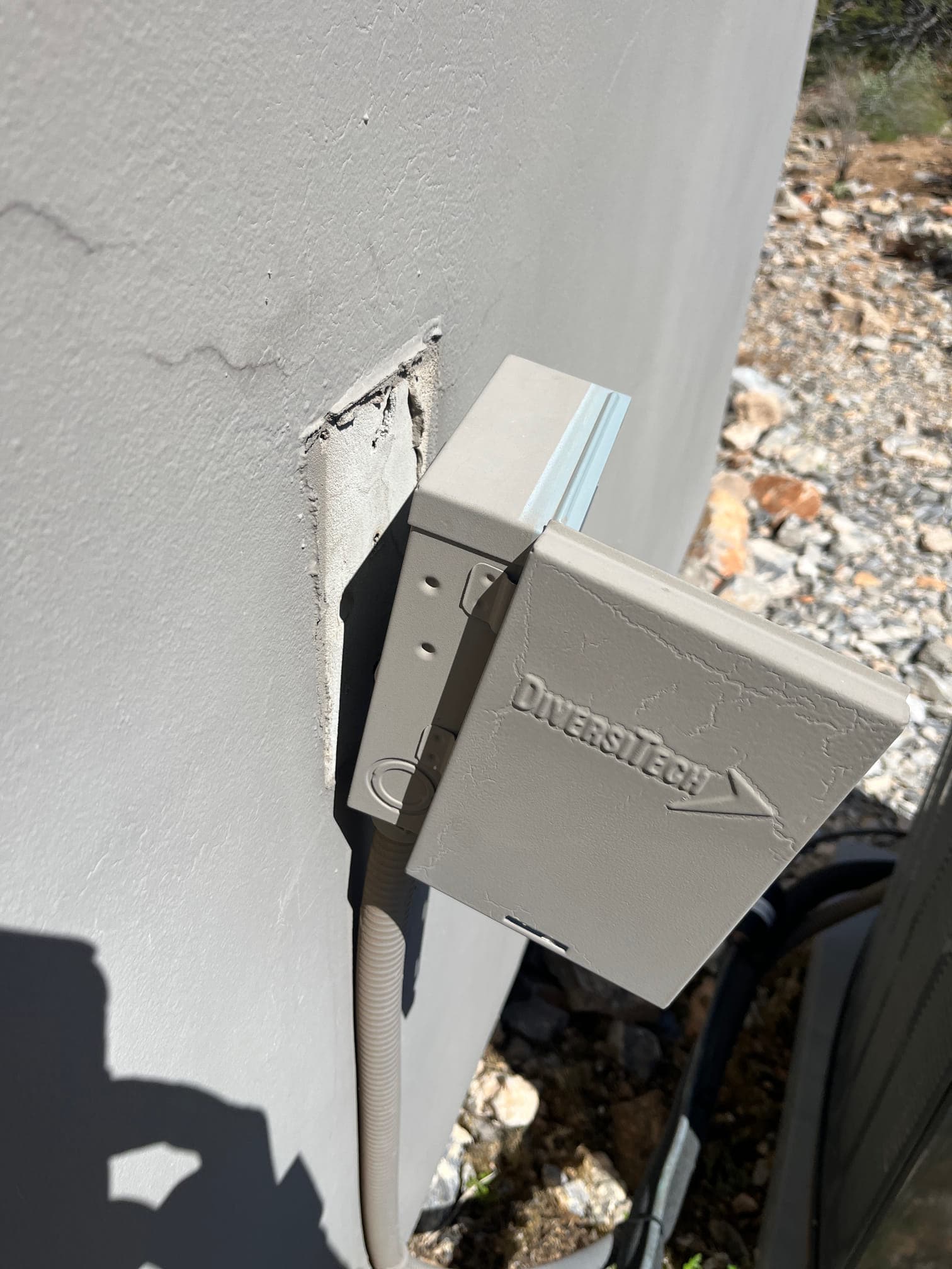 Outdoor electrical disconnect cover mounted on exterior wall beside the condenser unit, with flexible conduit entering the housing.