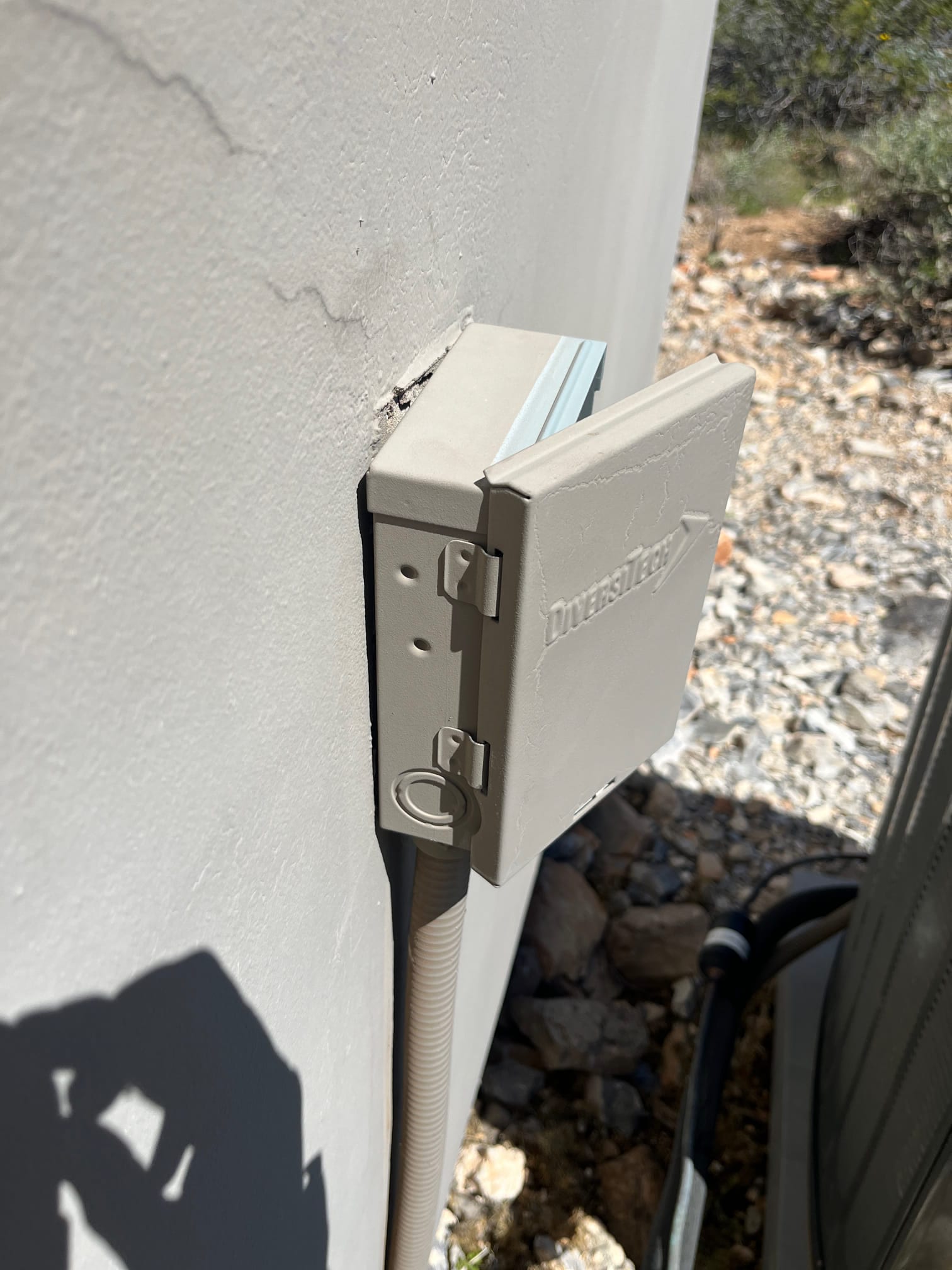 Outdoor HVAC disconnect box with open cover mounted on exterior wall beside the condenser and flexible conduit.