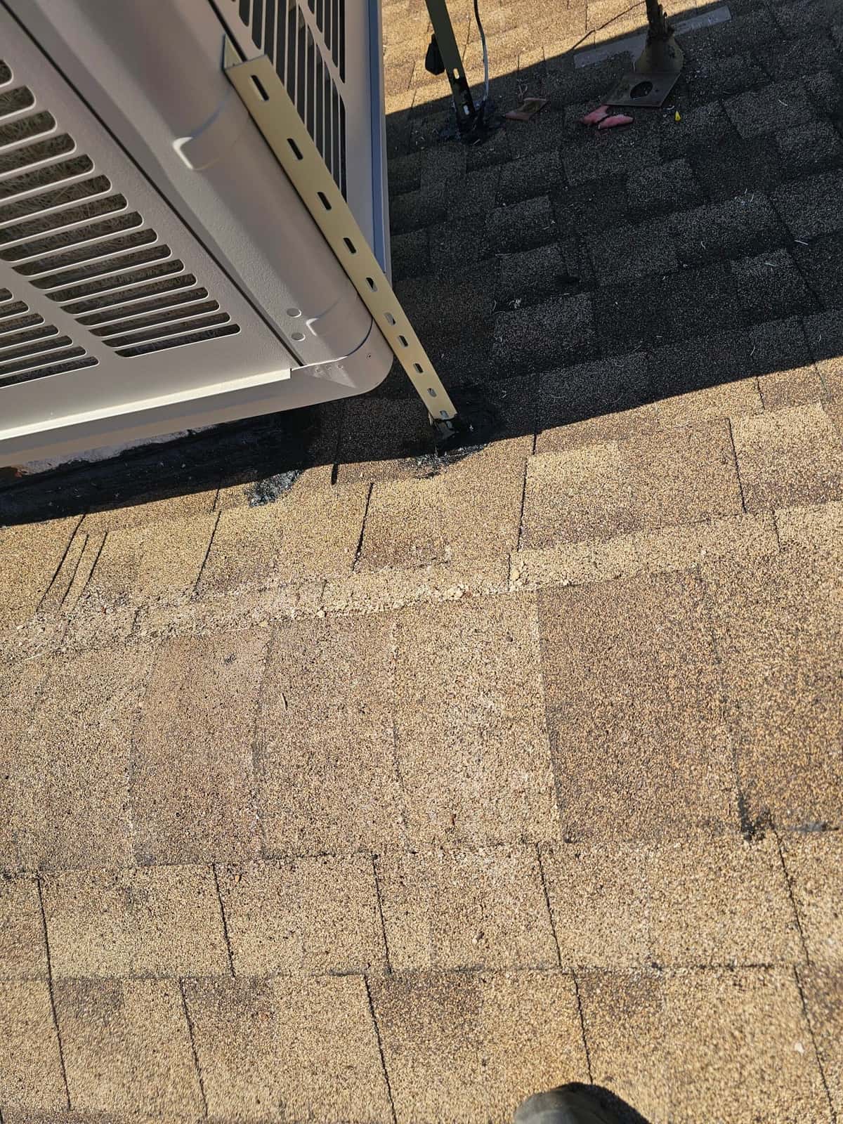 Outdoor HVAC unit mounted on a roof with a metal support bracket secured and sealed to the shingles.
