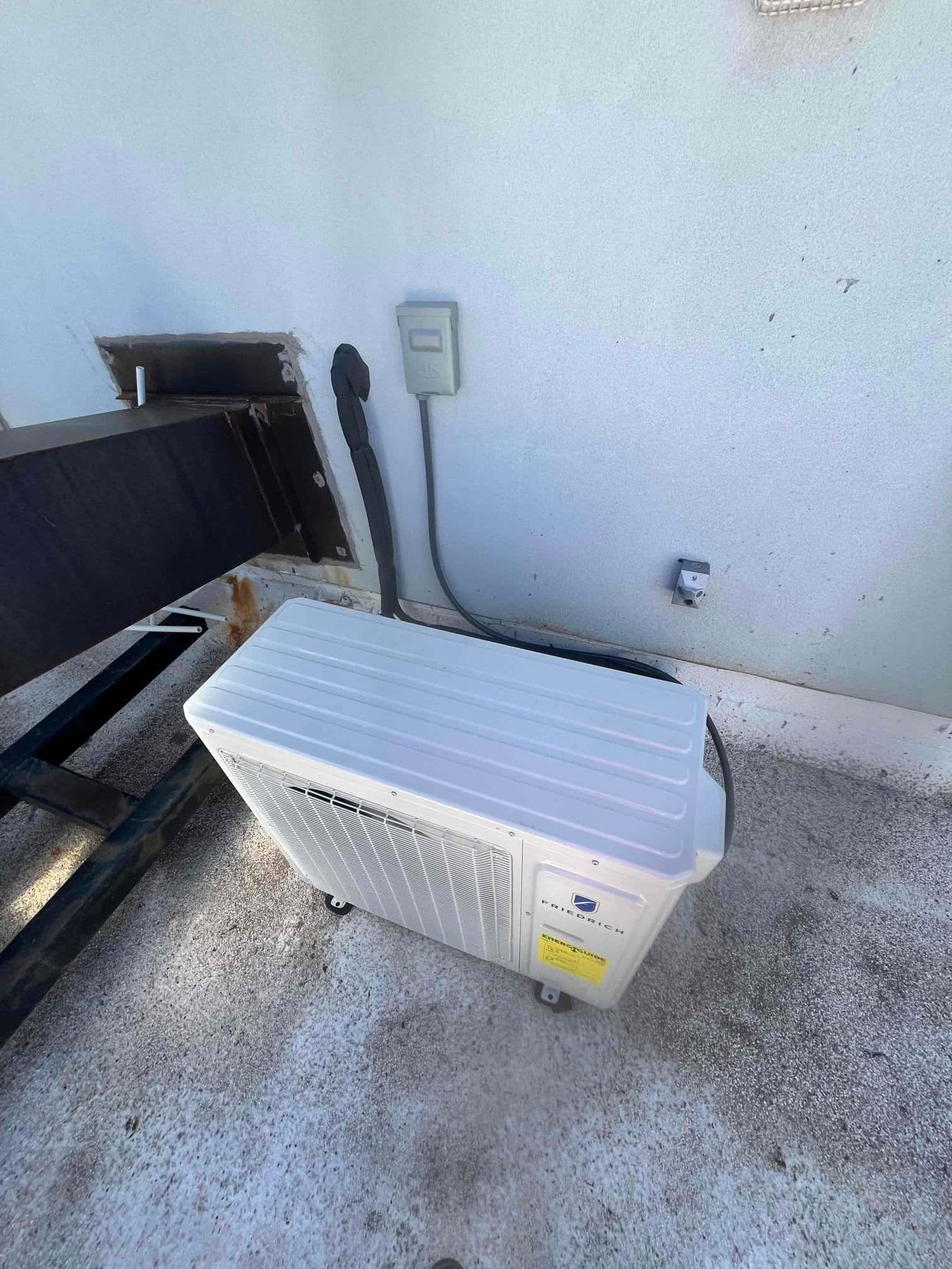 Outdoor mini-split condenser set on a rooftop surface with insulated line set penetration and weatherproof electrical disconnect mounted nearby.
