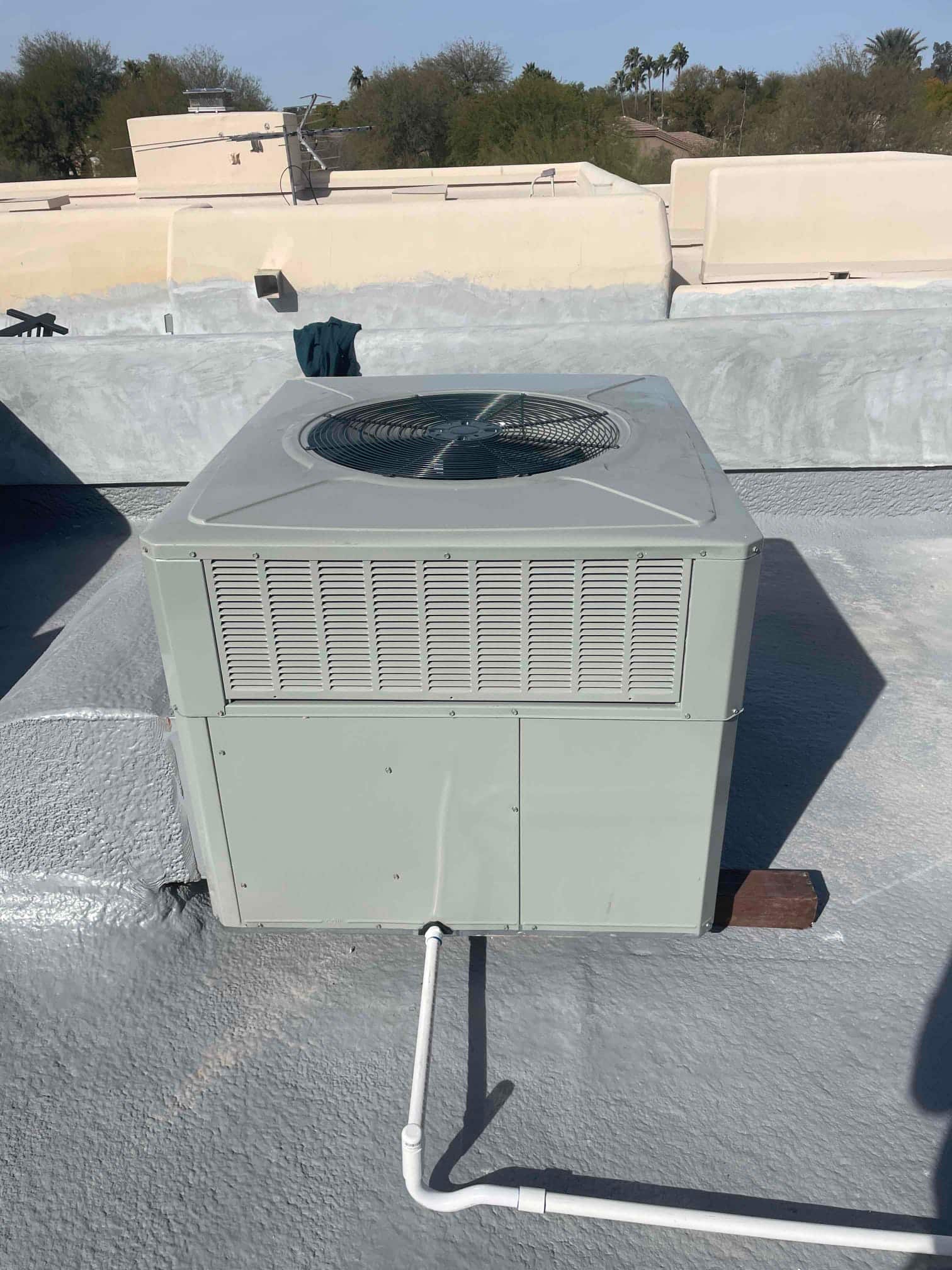 Packaged rooftop unit newly set on a coated roof with connected condensate drain piping and fan guard visible.