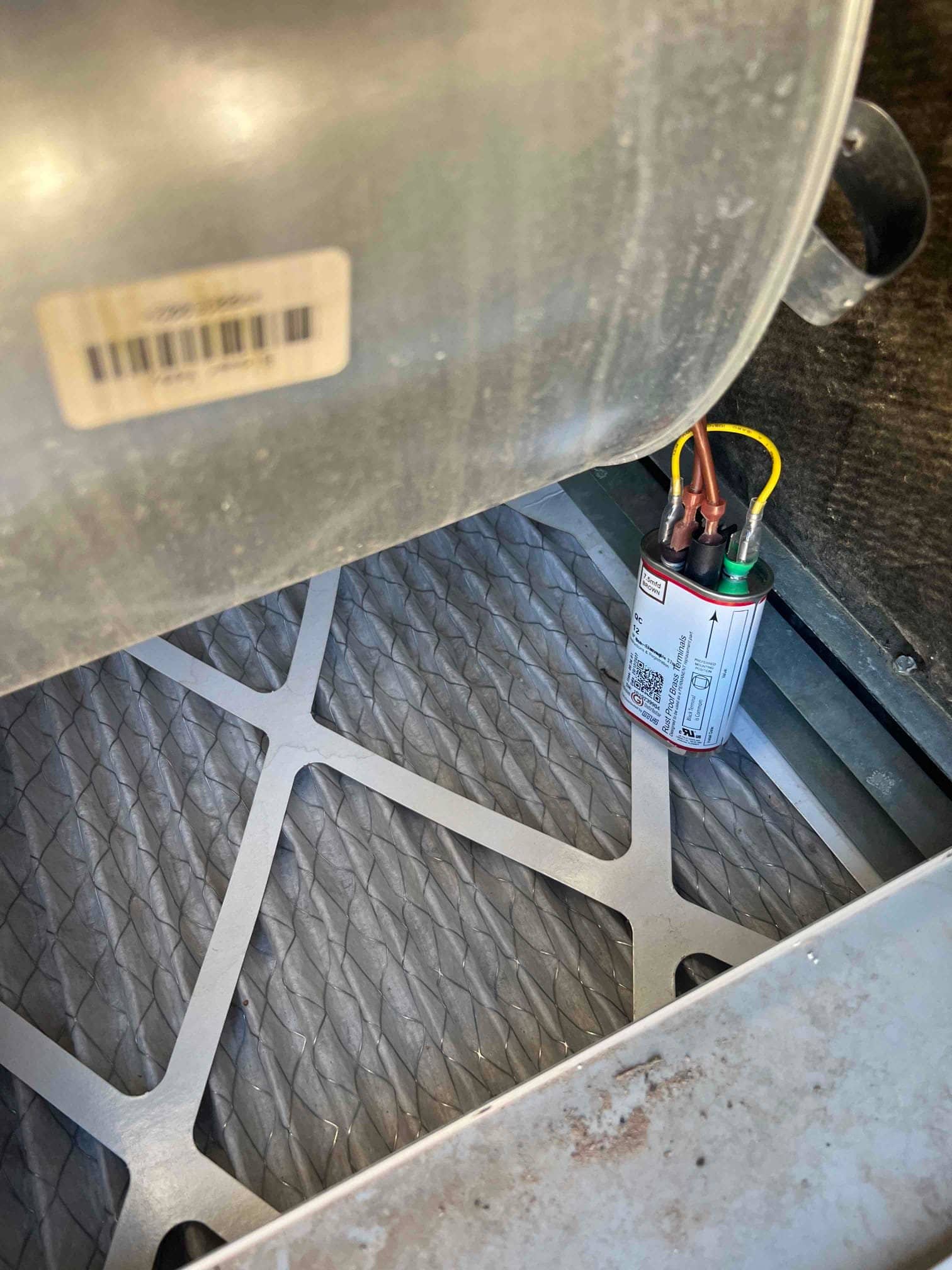 Pleated air filter below the blower housing, with a wired capacitor positioned inside the cabinet.