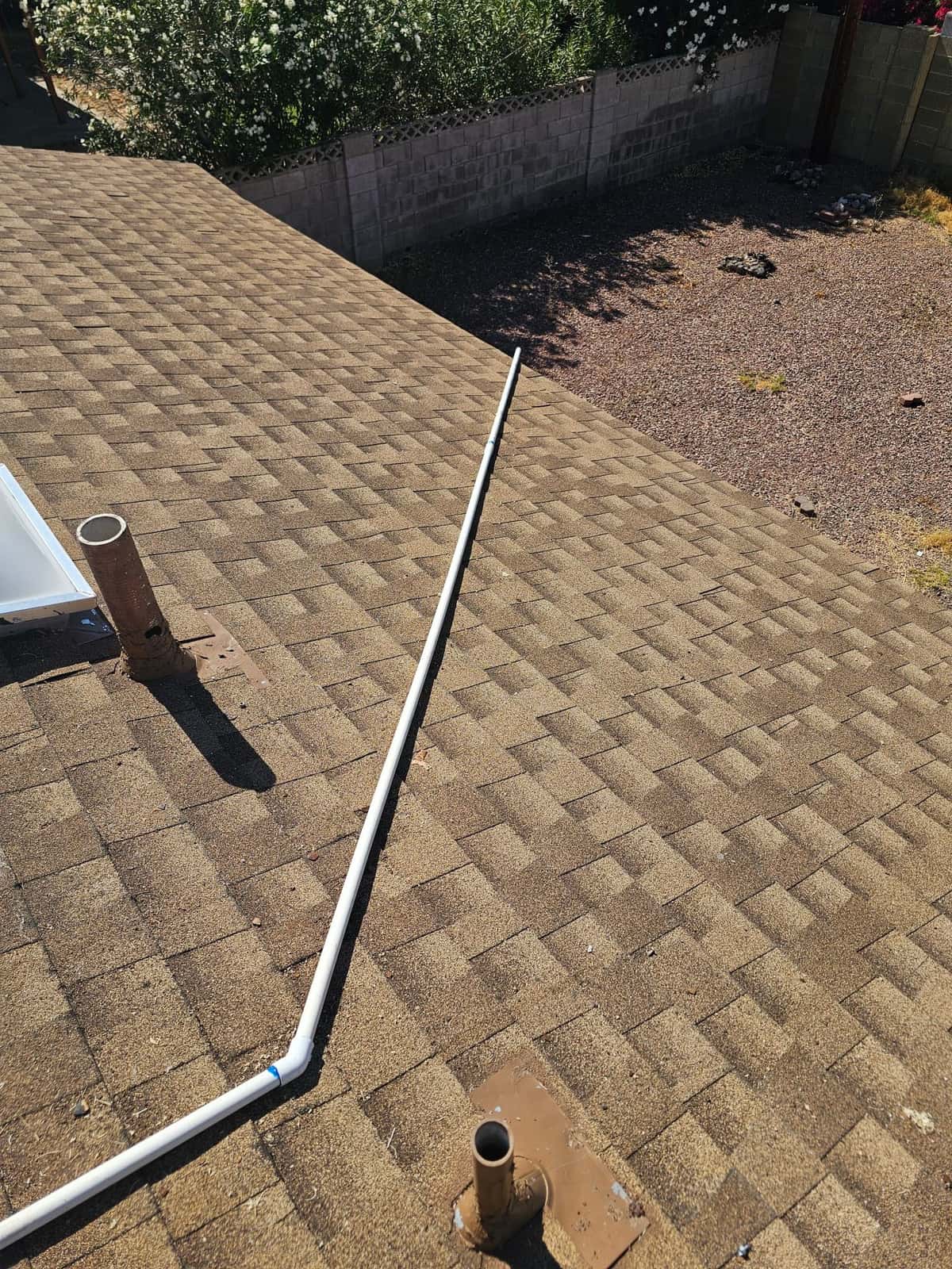PVC condensate drain line routed across the shingle roof with glued elbow fitting and roof penetrations nearby.