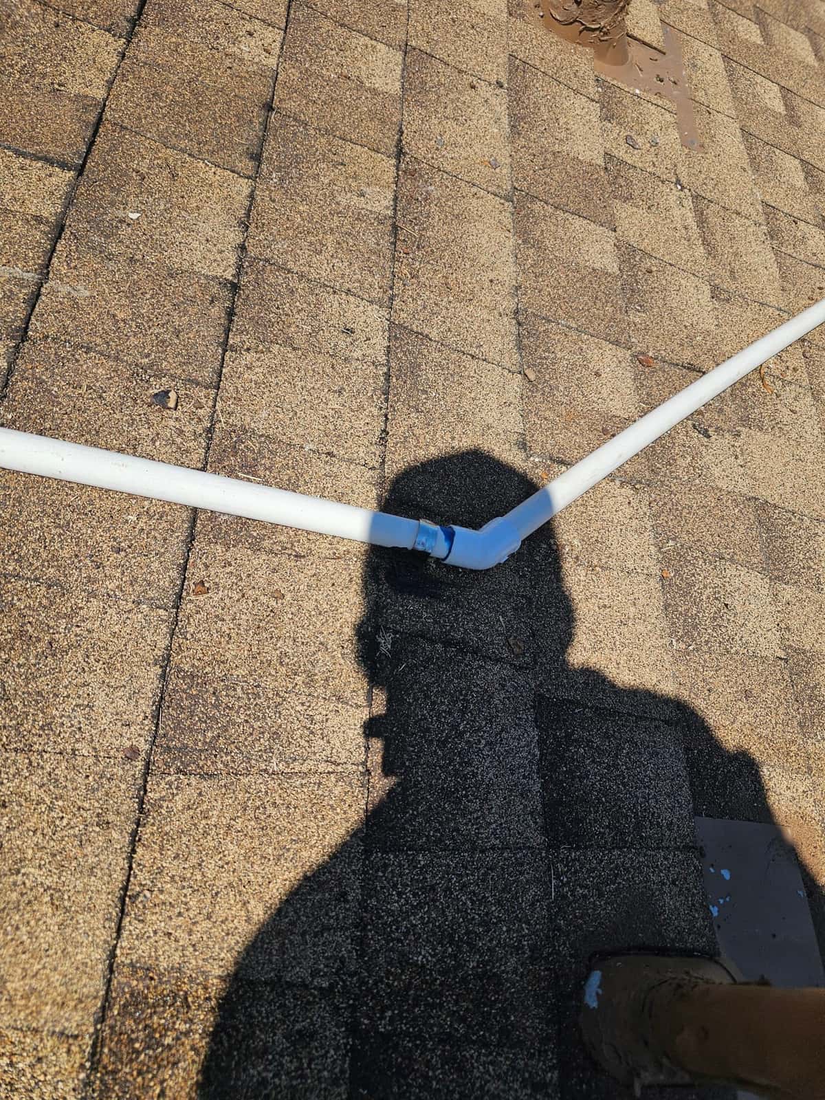 PVC drain line with an elbow fitting routed across roof shingles, shown during installation work for rooftop equipment.