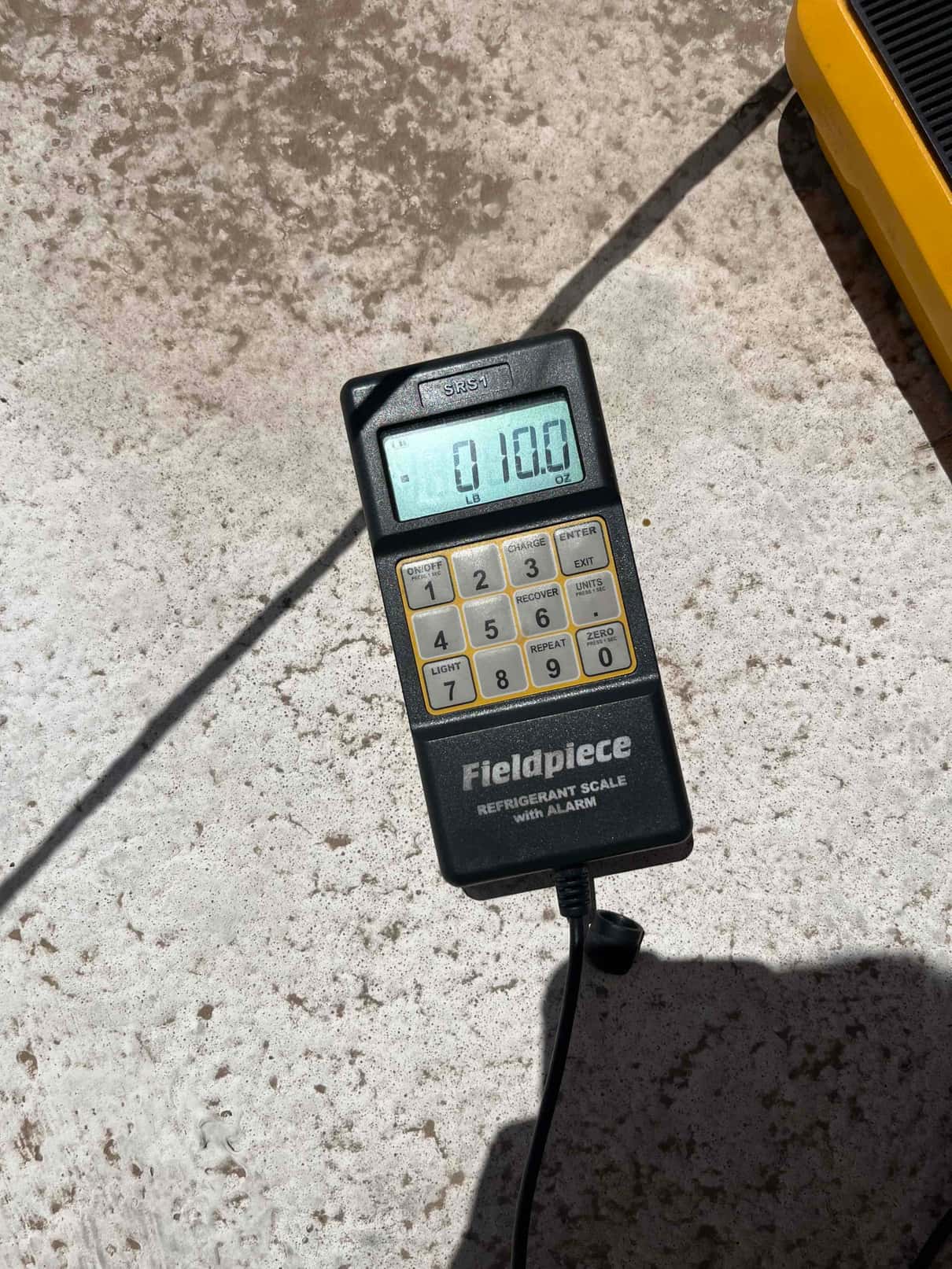 Refrigerant charging scale display shows 0.10 lb during R-410A recharge, with keypad and cable visible on the job site.