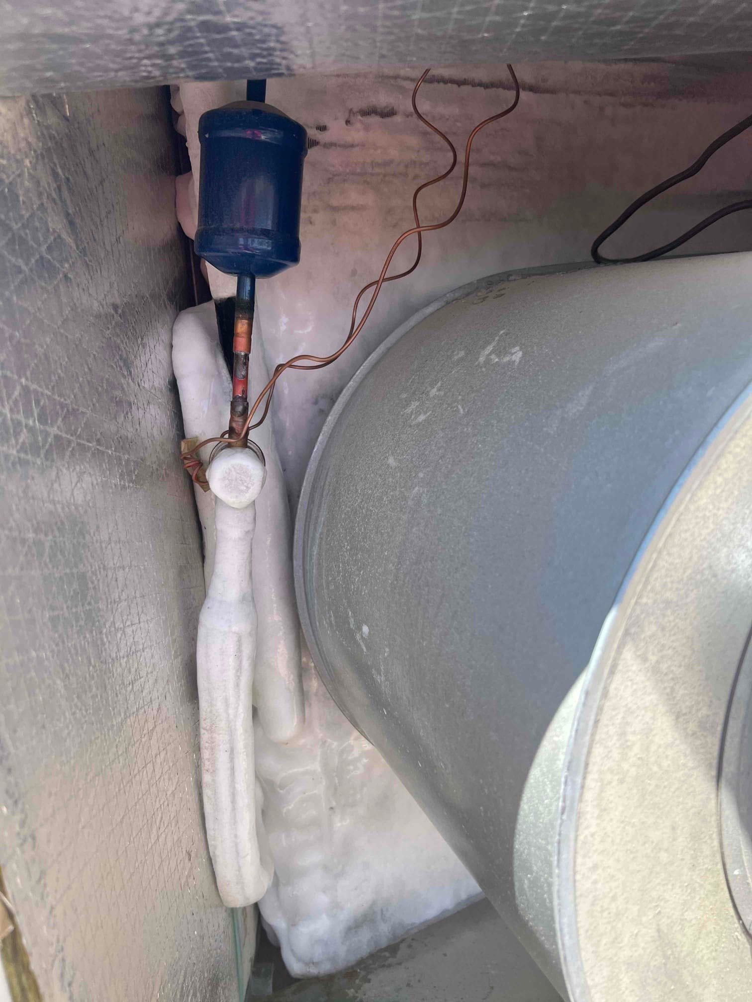 Refrigerant line and fittings inside the condenser cabinet show heavy ice buildup next to the compressor housing.