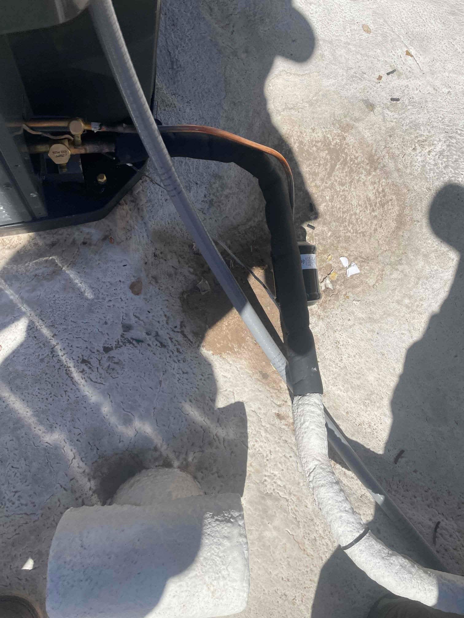 Refrigerant lines and electrical whip connected to the outdoor condenser, with insulation and taped joints at the unit entry.