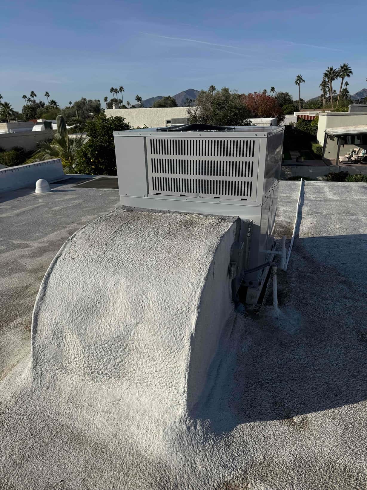 Rooftop packaged heat pump set on a curb, with sealed roof penetration and duct curb visible in sunlight.