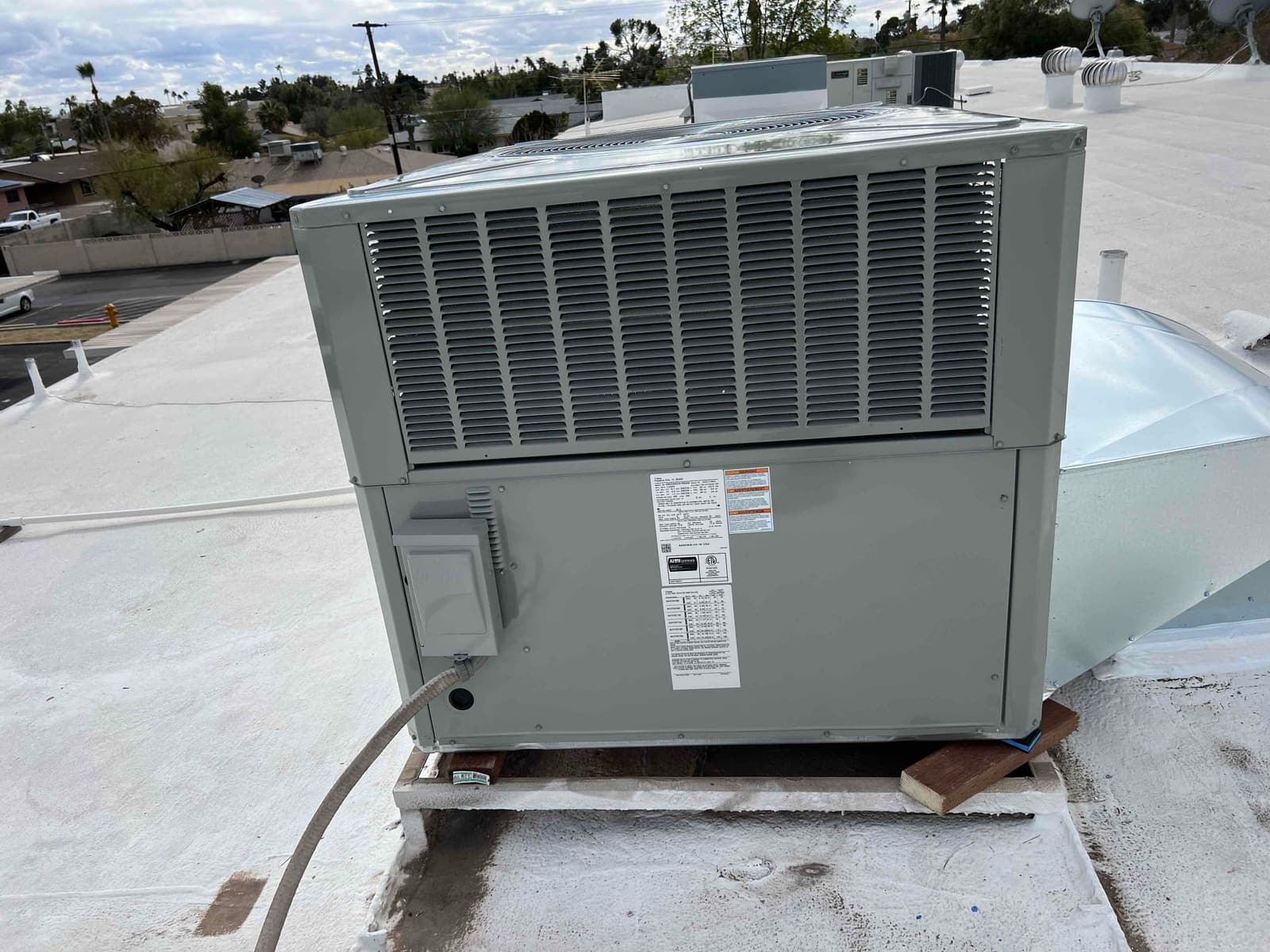Rooftop packaged HVAC unit installed on curb with connected electrical disconnect and sealed duct transition on a flat roof.