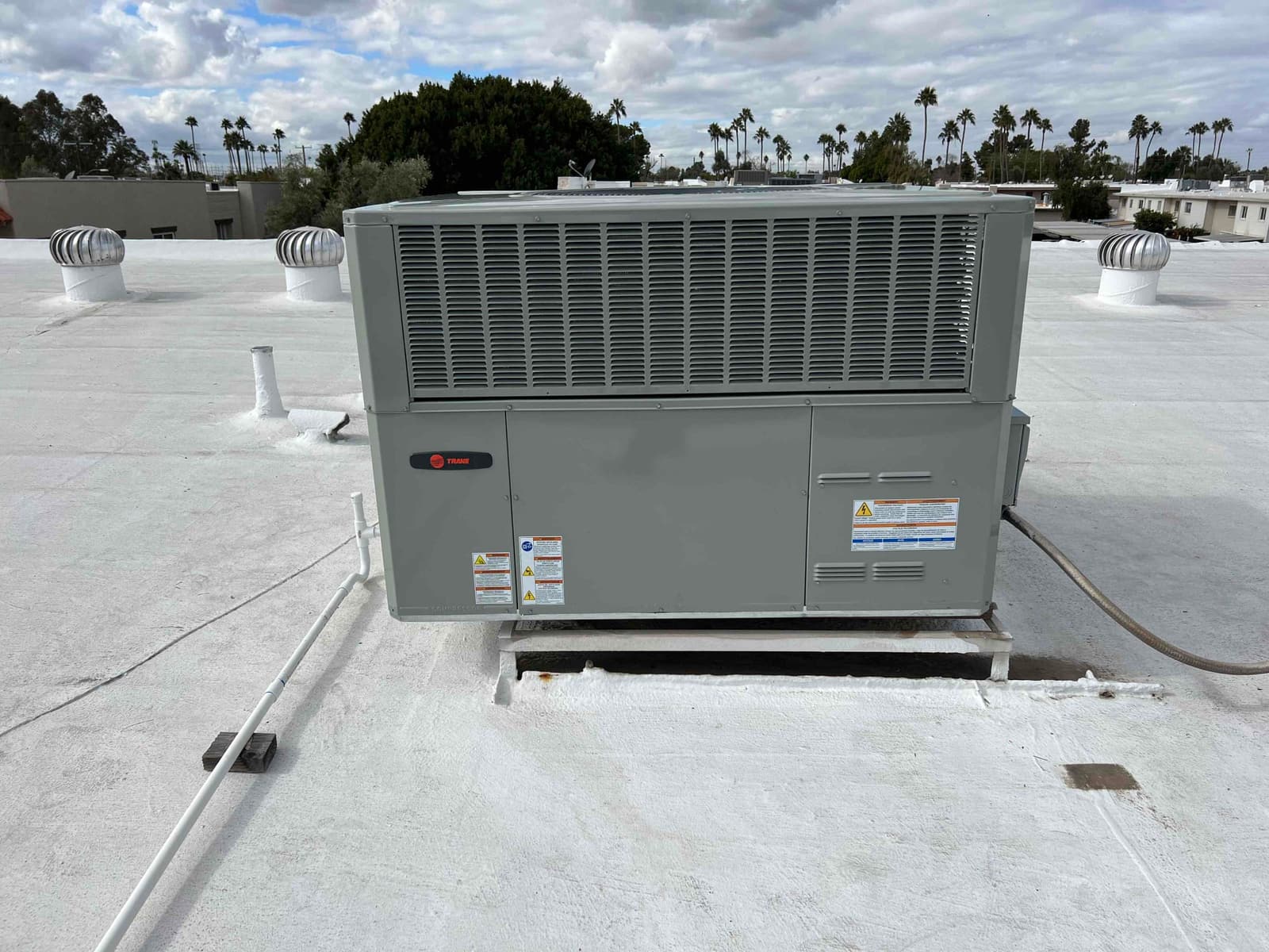 Rooftop packaged HVAC unit newly set on a curb with connected condensate drain and sealed roof penetrations.