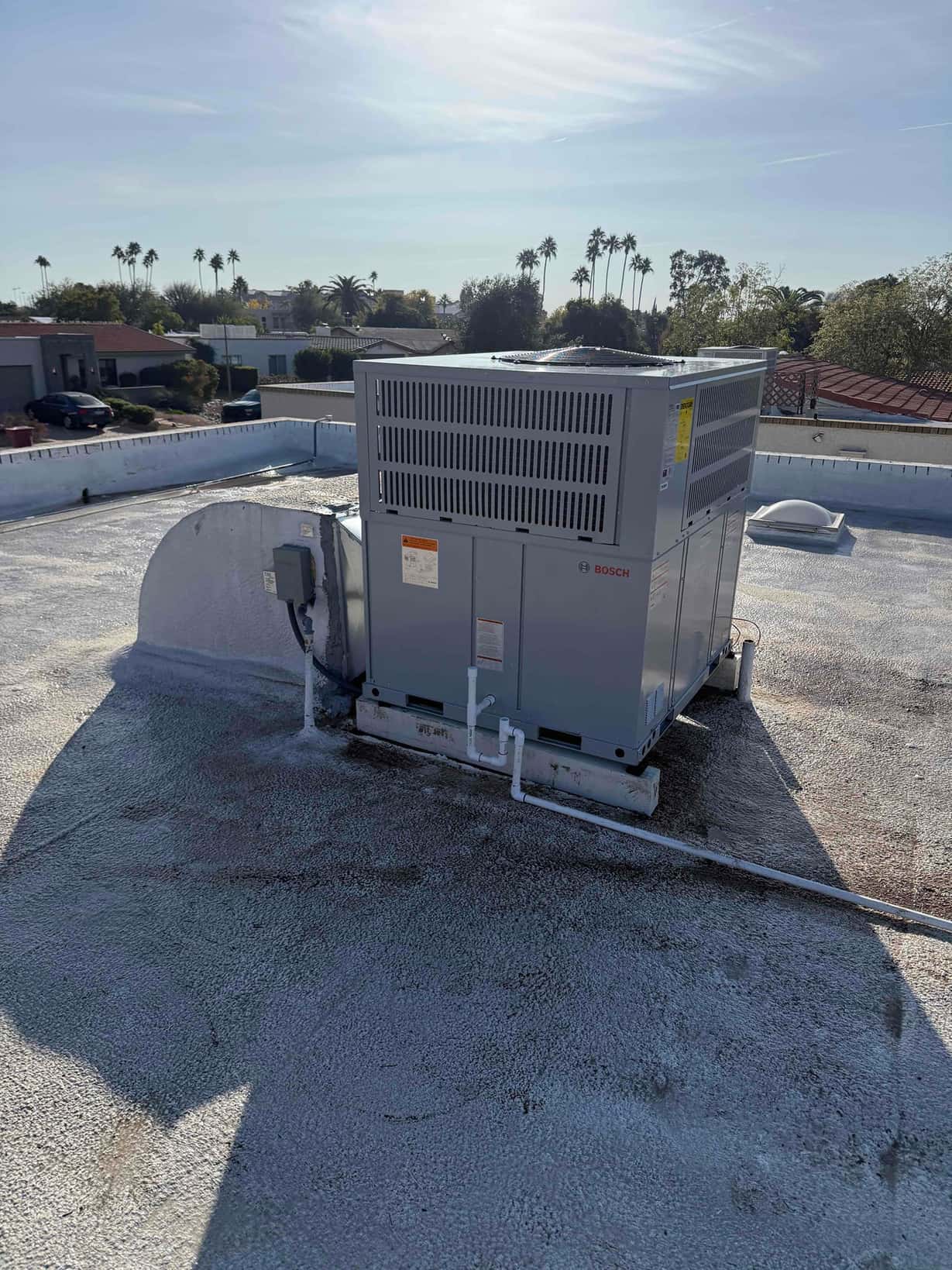 Rooftop packaged HVAC unit newly set on curb with connected electrical whip and PVC condensate drain routing across the roof.