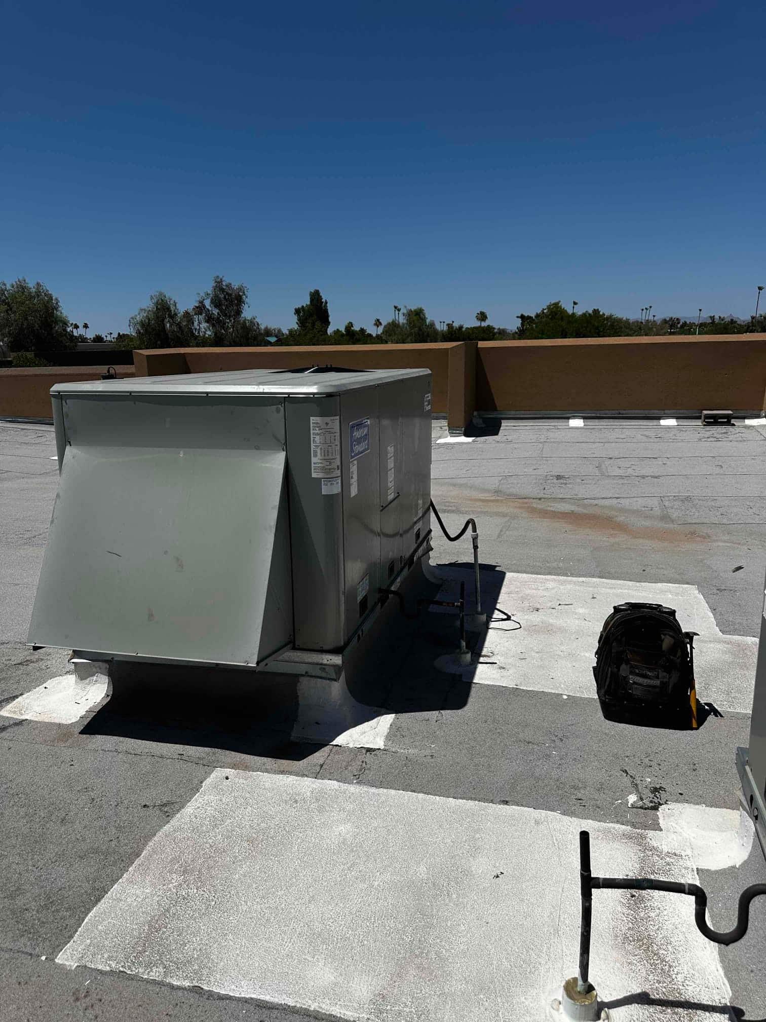 Rooftop packaged HVAC unit set on curb with connected refrigerant lines and service tools nearby during installation.