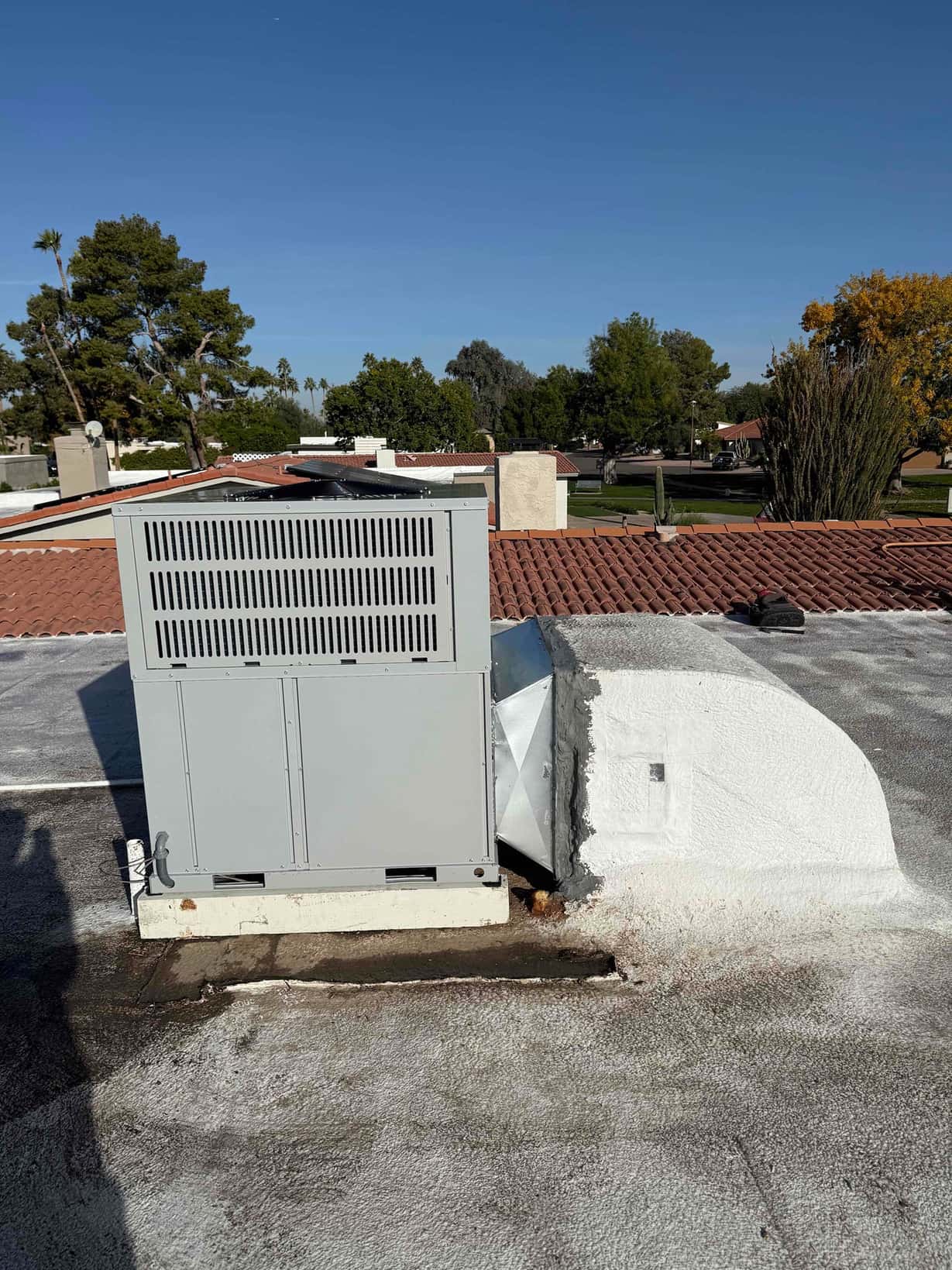 Rooftop packaged HVAC unit set on a curb with sealed duct transition and roofing around the base.