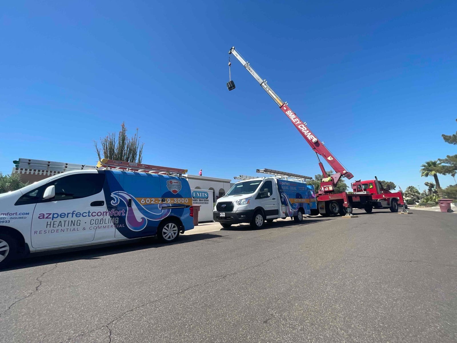 Service vans and a crane stage at the job site to lift HVAC equipment during the installation project.