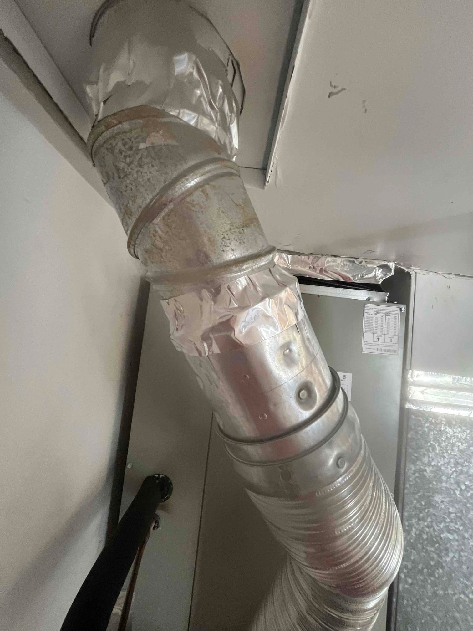 Sheet-metal ductwork connected to the air handler with sealed joints and foil tape, showing the return and supply transitions.