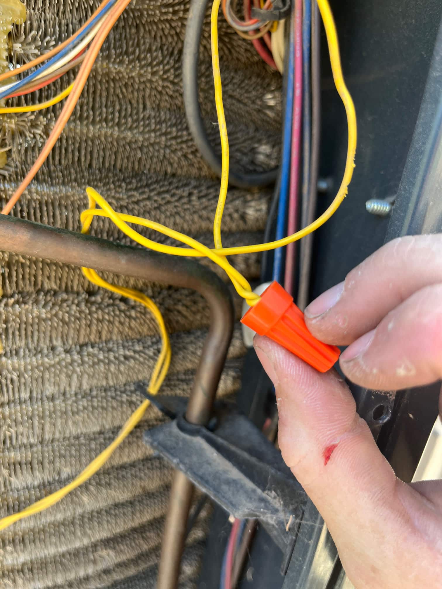 Technician holds an orange wire connector joining yellow control wires near the condenser coil and copper refrigerant line.