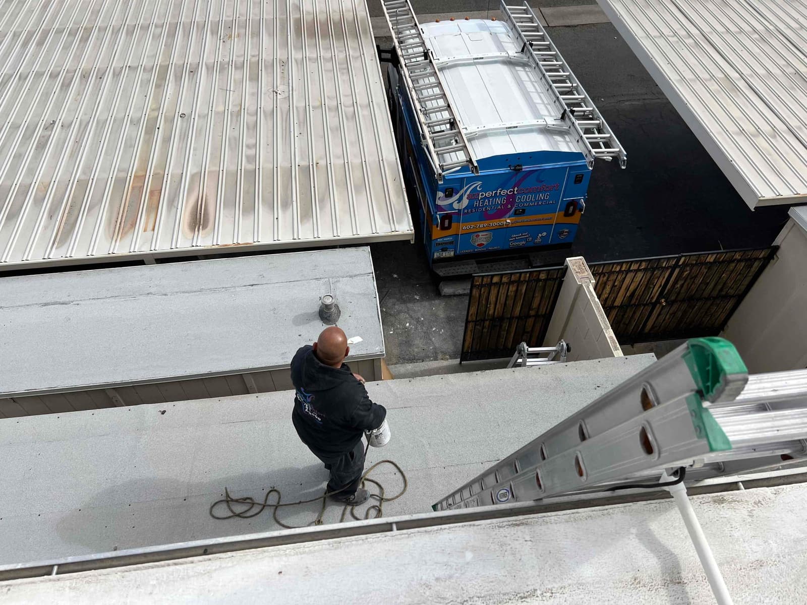 Technician on a rooftop near a ladder and service vehicle during an HVAC installation site setup.