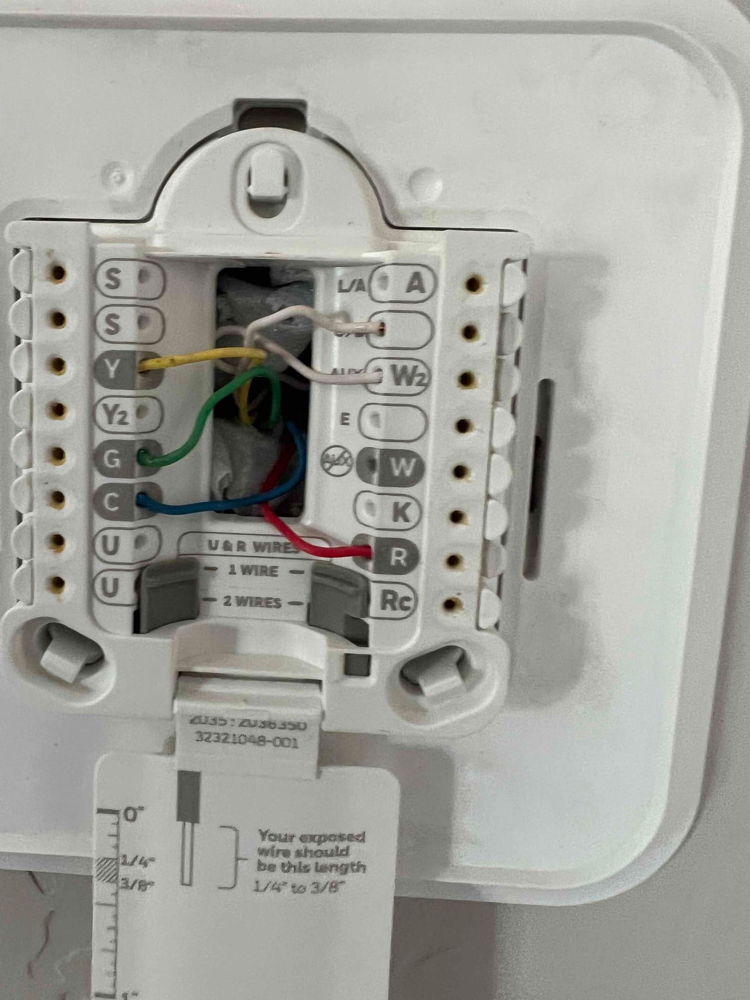 Thermostat sub-base with labeled terminals and connected red, blue, green, yellow, and white control wires visible inside the wall opening.