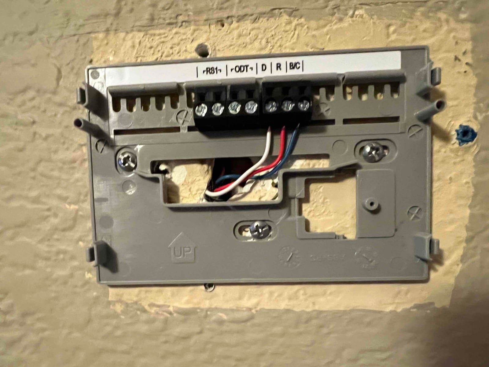 Thermostat wall plate installed with control wires landed on labeled terminals and mounting screws secured to the wall.