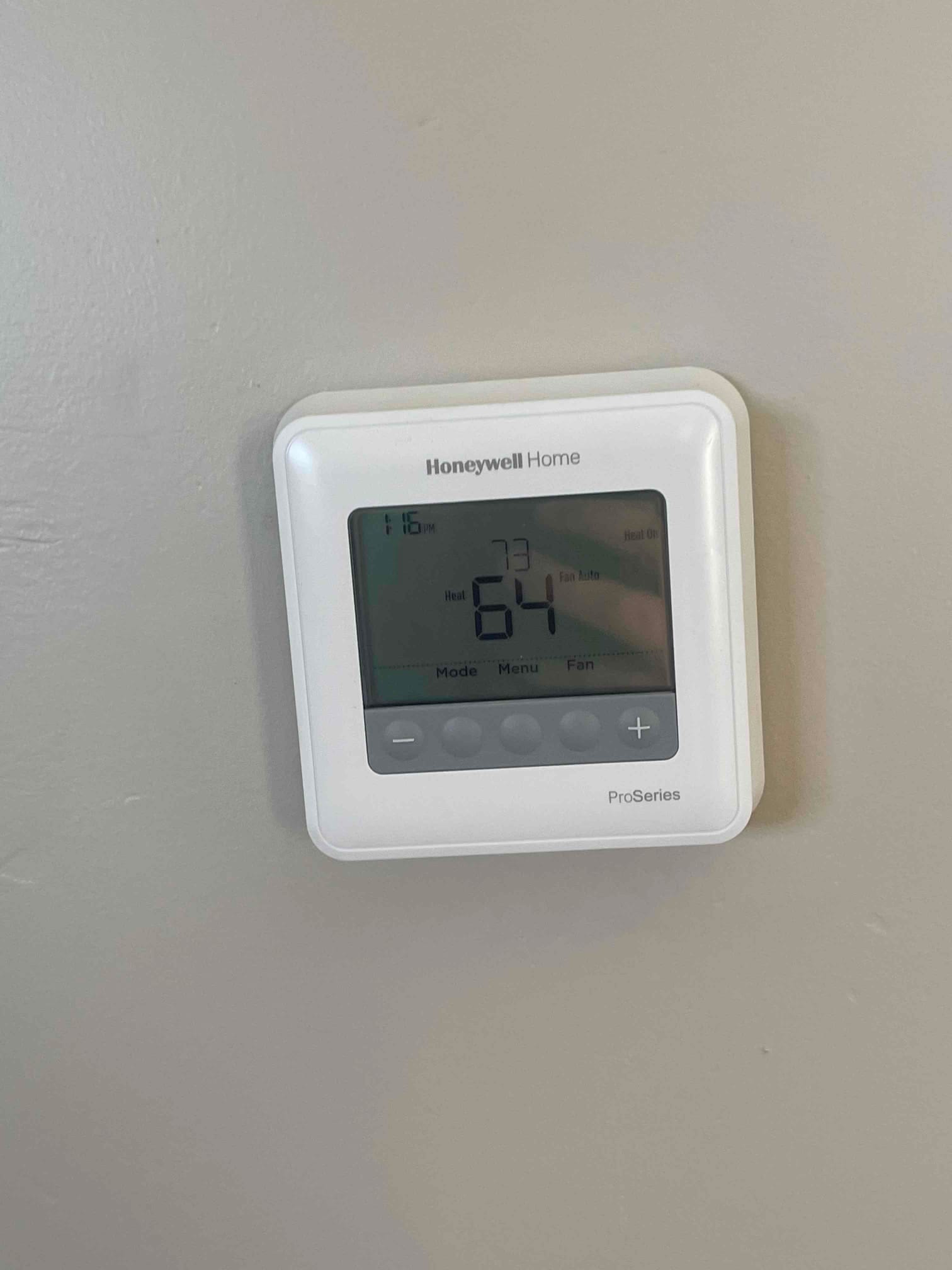 Wall-mounted digital thermostat installed and powered, displaying current room temperature and control buttons.