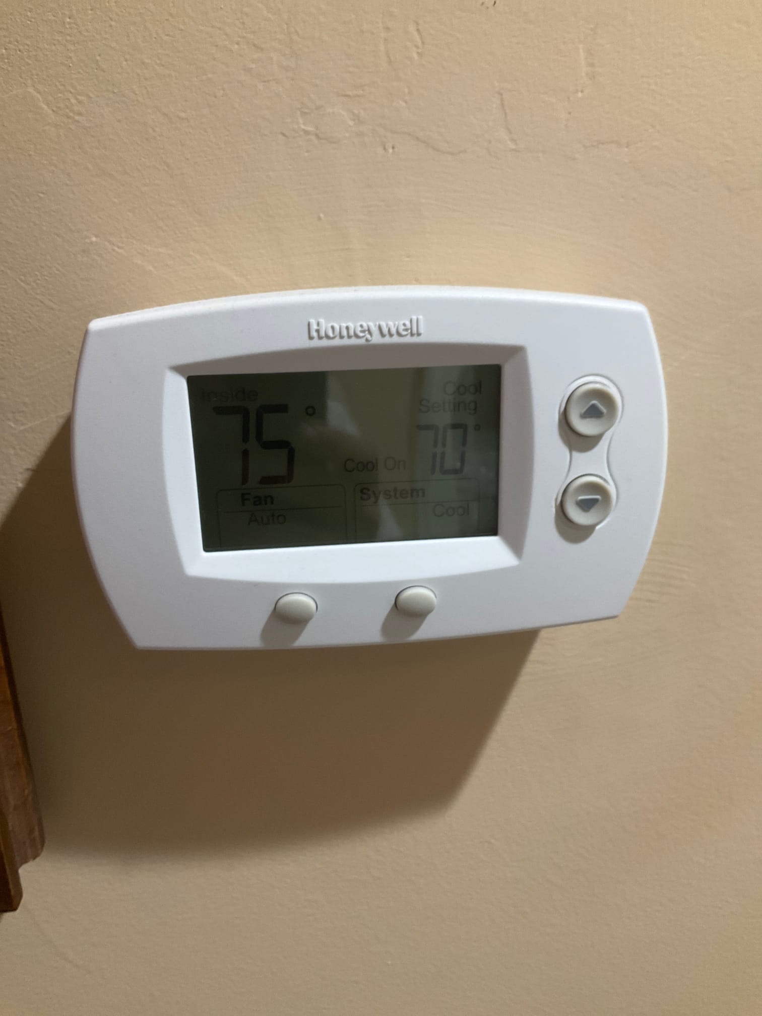 Wall-mounted digital thermostat shows inside 75°F and cool setpoint 70°F, system on cool with fan auto.