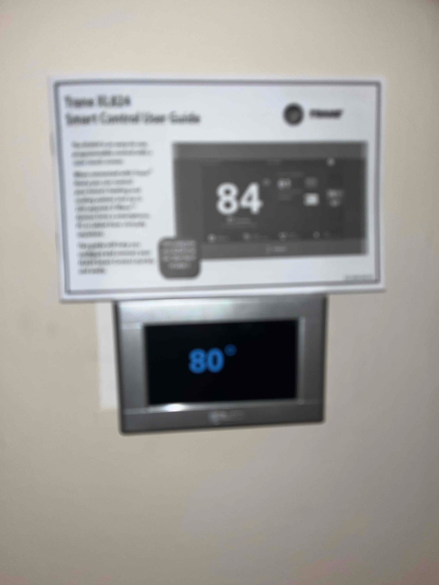 Wall-mounted smart thermostat displays 80 degrees after installation, with the user guide shown above the device.