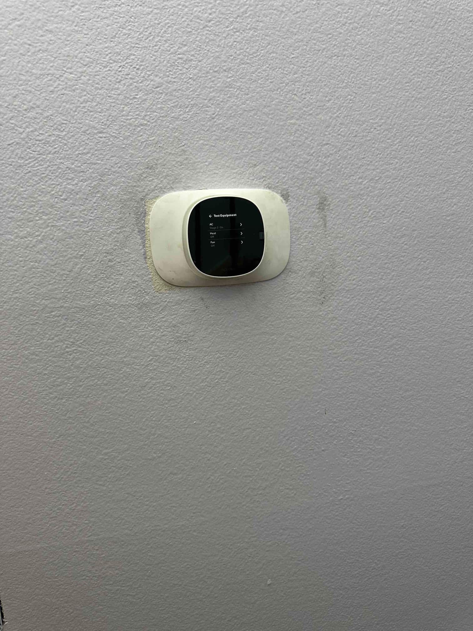 Wall-mounted smart thermostat installed and displaying a test menu for AC and heat functions after system setup.
