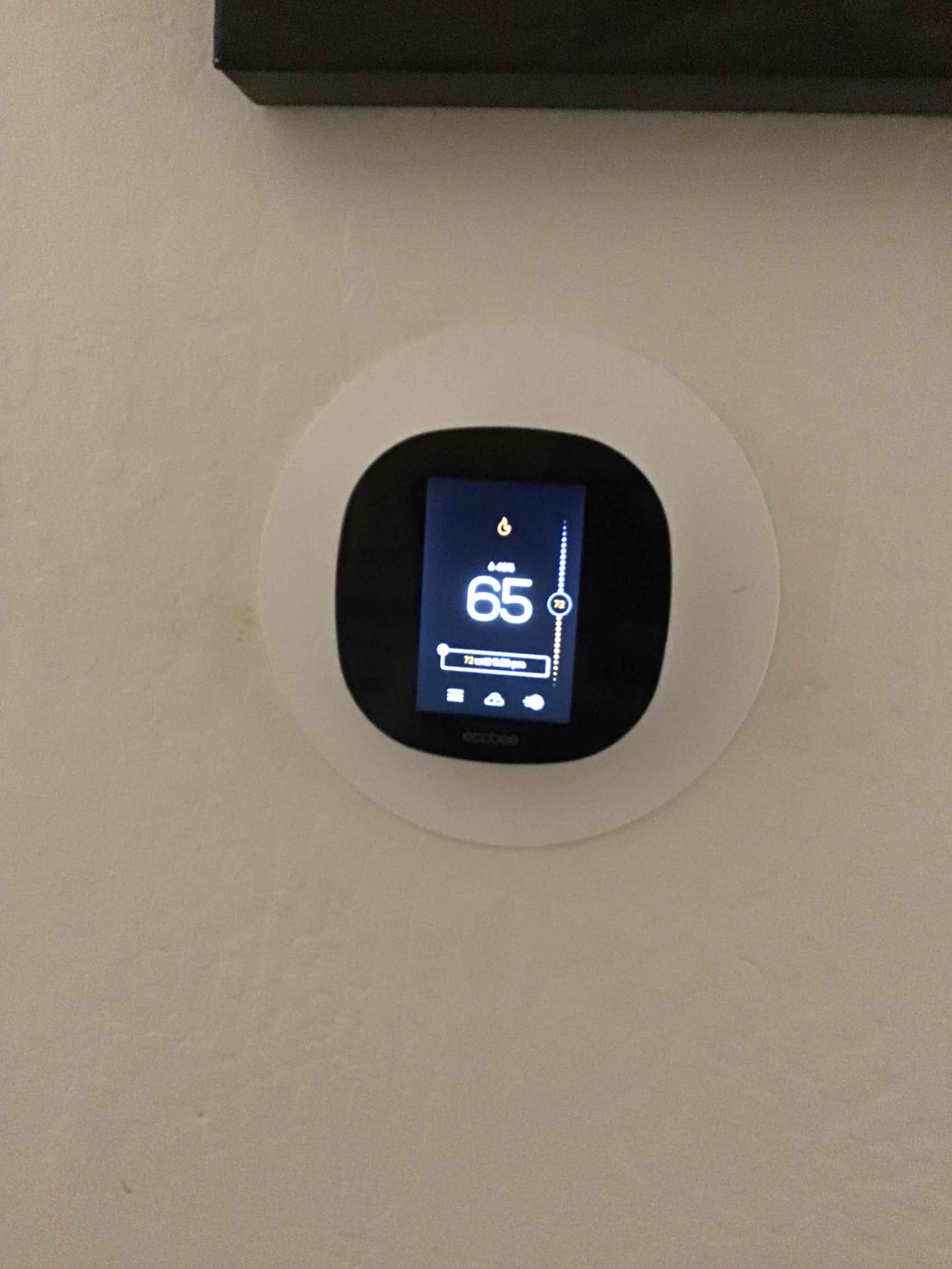 Wall-mounted smart thermostat installed with trim plate, screen illuminated and showing indoor temperature and control interface.