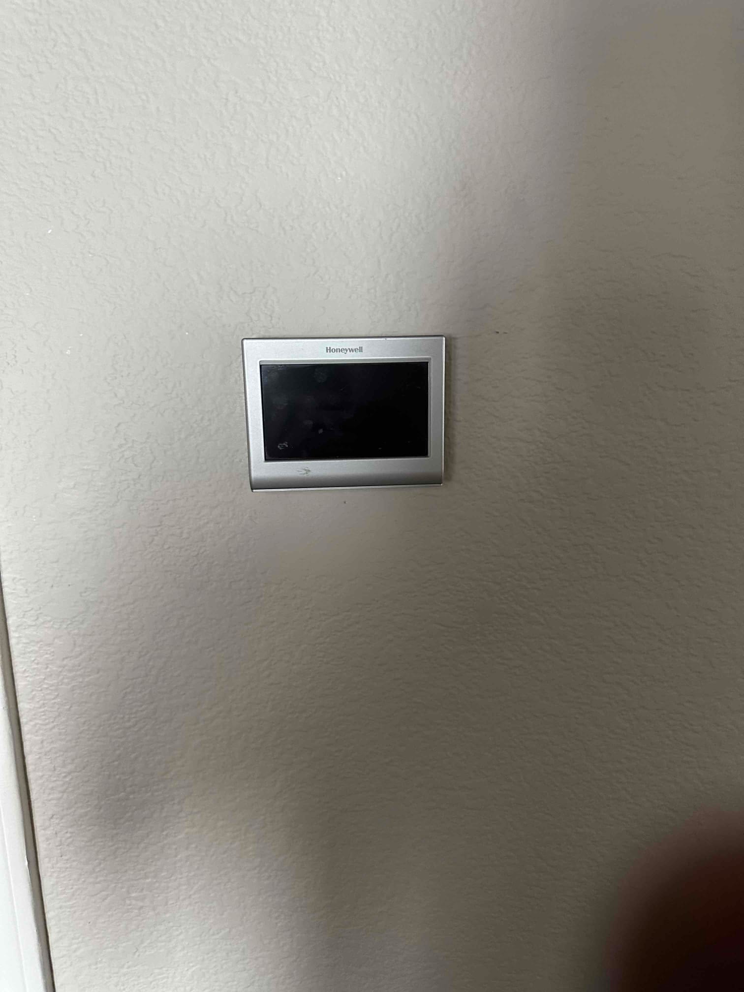 Wall-mounted thermostat with blank display installed on a finished interior wall near a doorway trim.