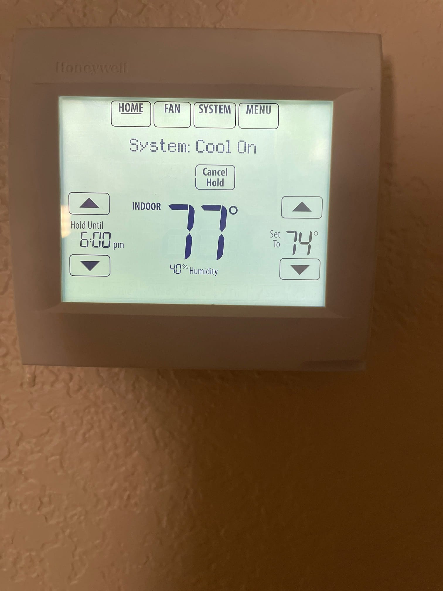 Wall-mounted thermostat display shows System Cool On, indoor 77°, setpoint 74°, 40% humidity, and a hold scheduled until 6:00 pm.