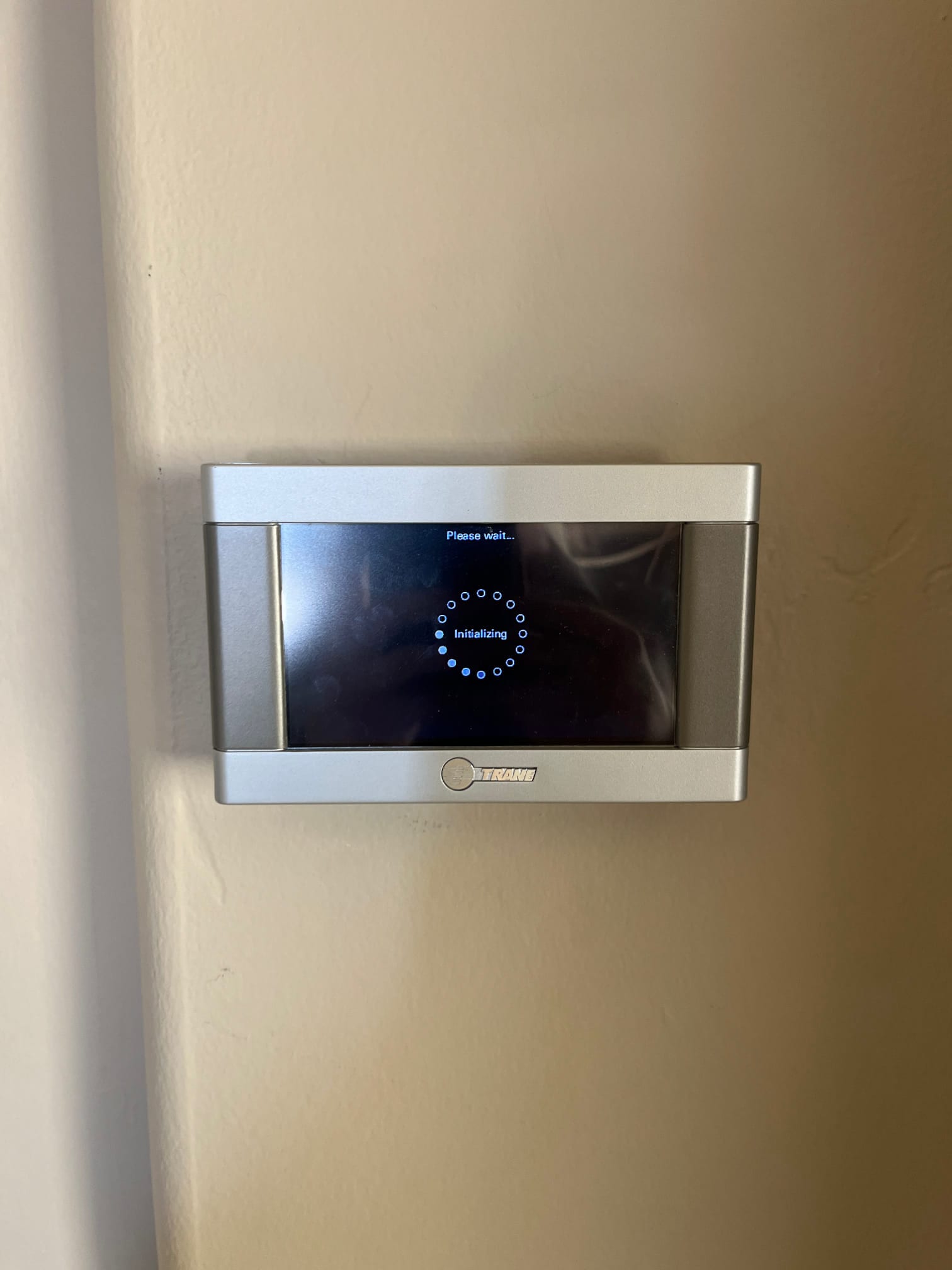 Wall-mounted thermostat displays an initializing screen with a loading indicator during system startup.