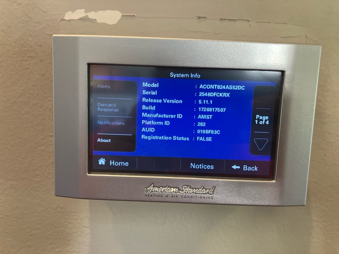 Wall-mounted thermostat displays system information screen with model, serial, firmware version, and navigation buttons visible.
