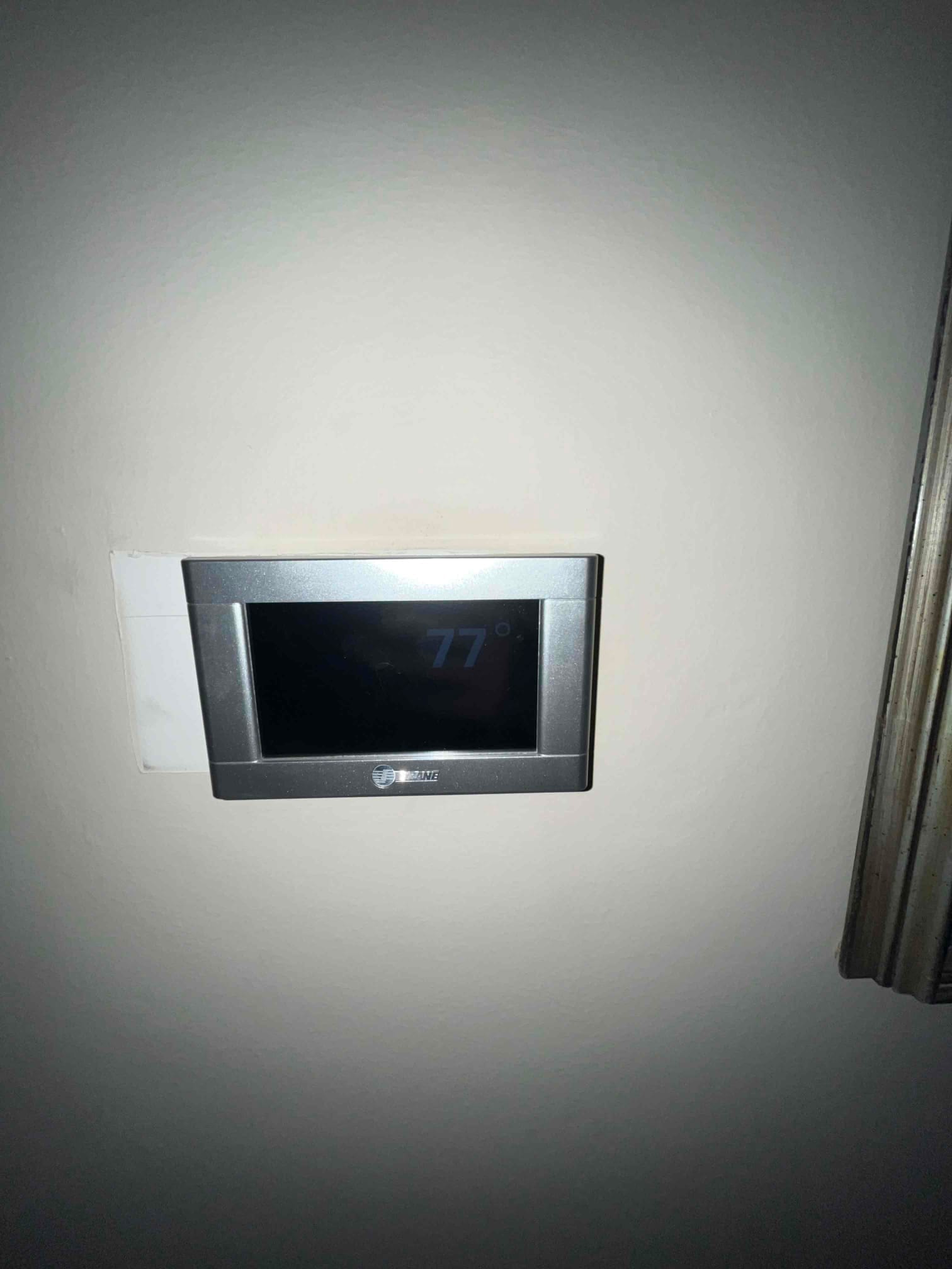 Wall-mounted thermostat installed and powered on, displaying a room temperature reading of 77 degrees.