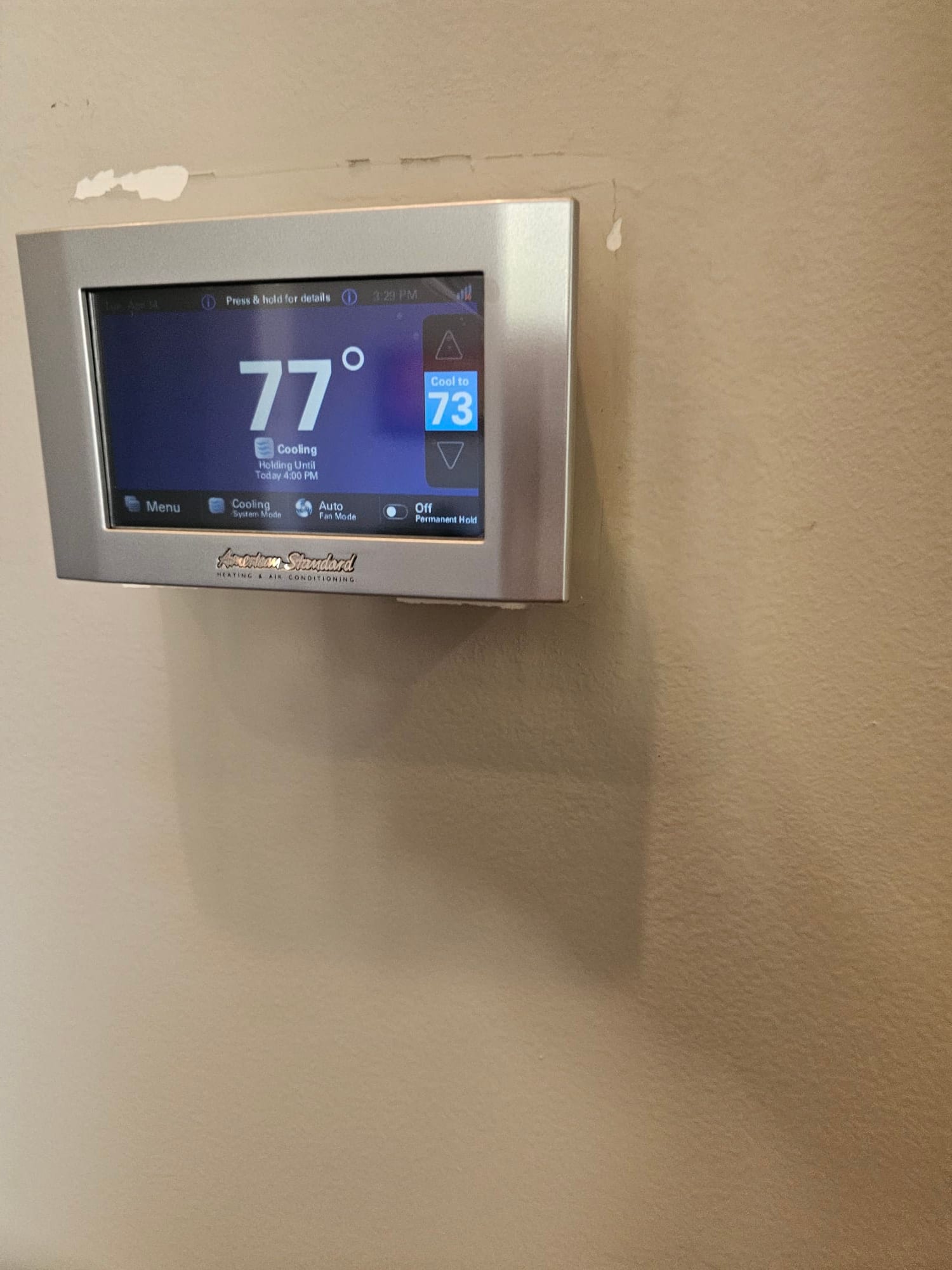 Wall-mounted touchscreen thermostat displays 77 degrees with cooling mode active and a setpoint of 73 degrees.