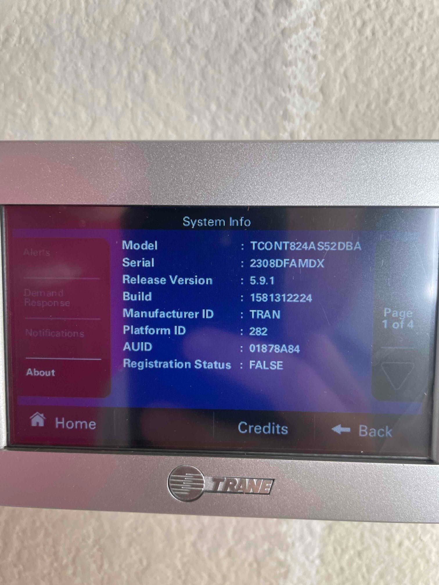 Wall-mounted touchscreen thermostat displays system information menu after installation, showing software version and device identifiers.