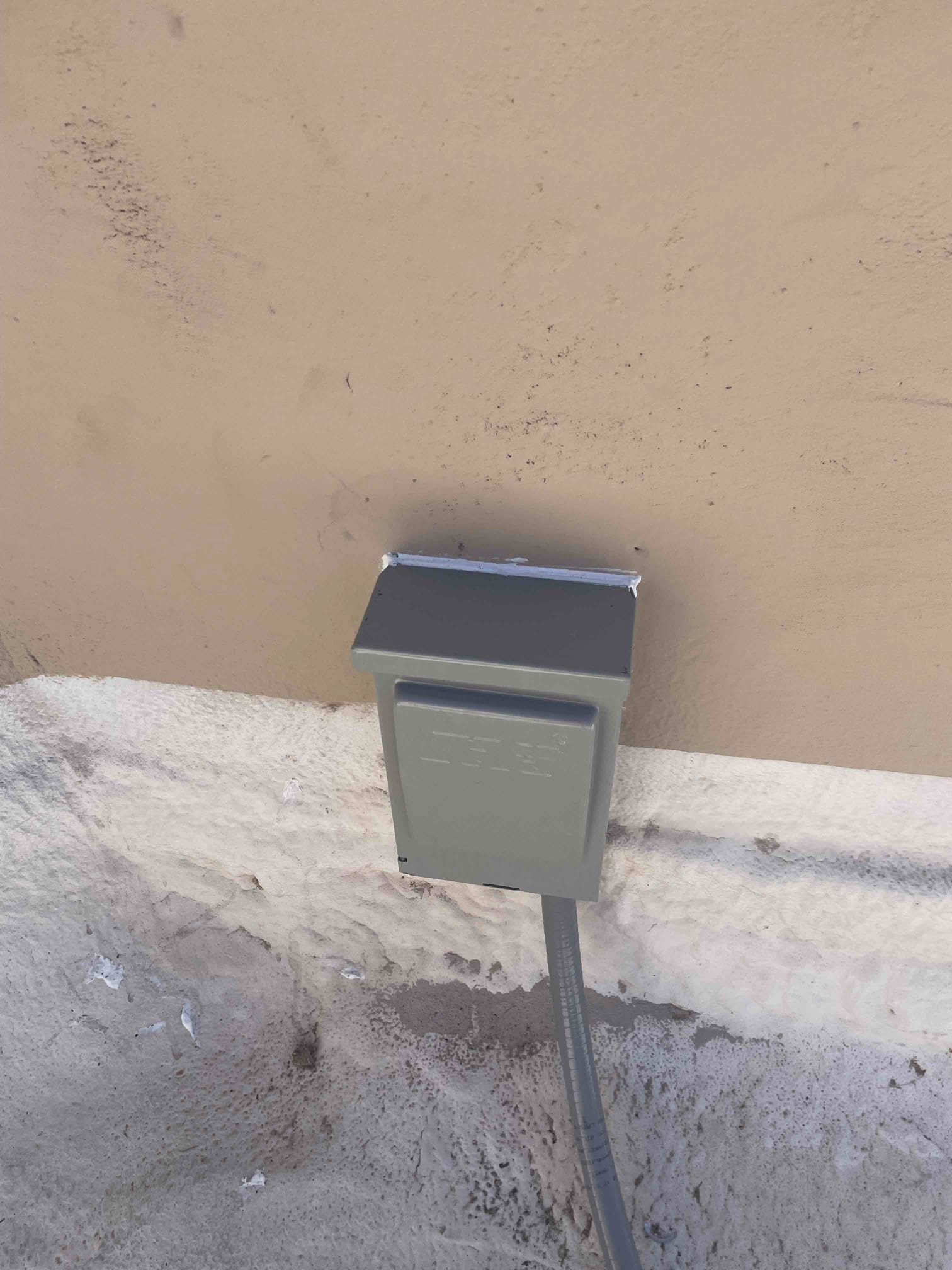 Weatherproof electrical disconnect box mounted on exterior wall with flexible conduit routed to the new HVAC condenser location.