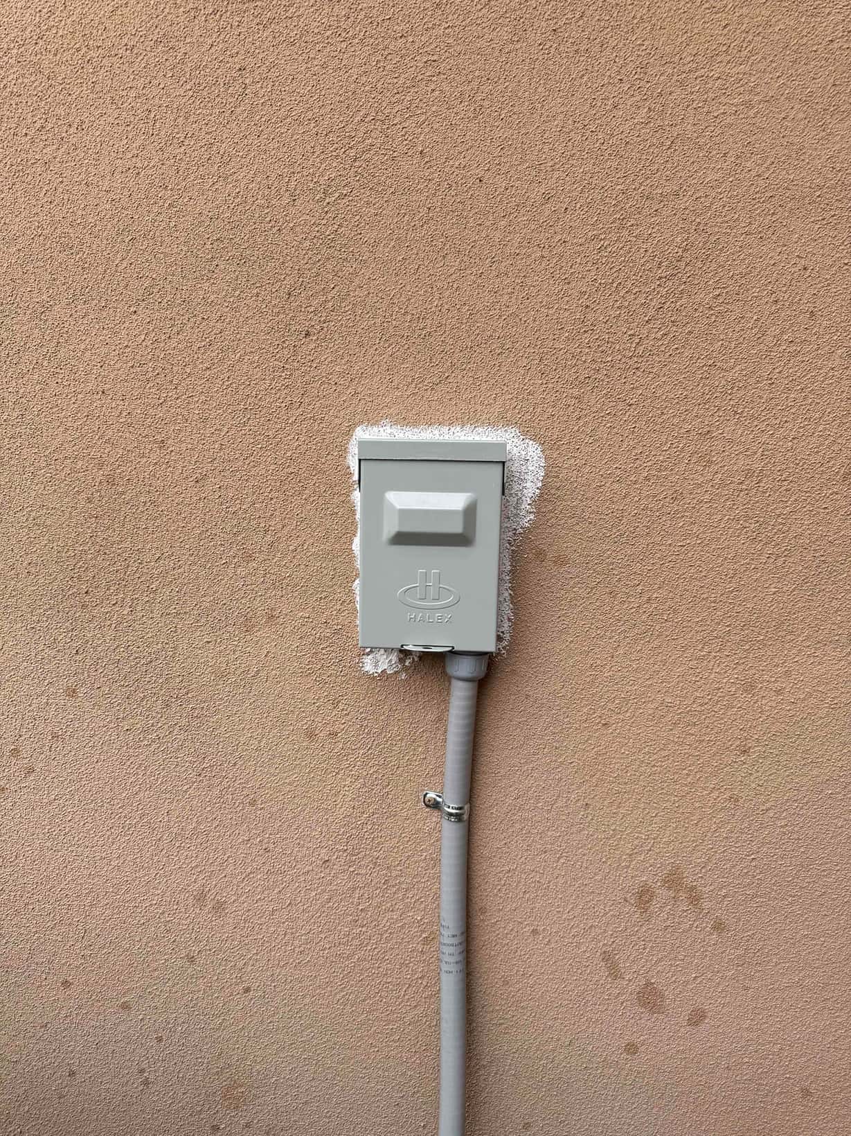 Weatherproof electrical disconnect box mounted on exterior wall with sealed penetration and secured flexible conduit routing.