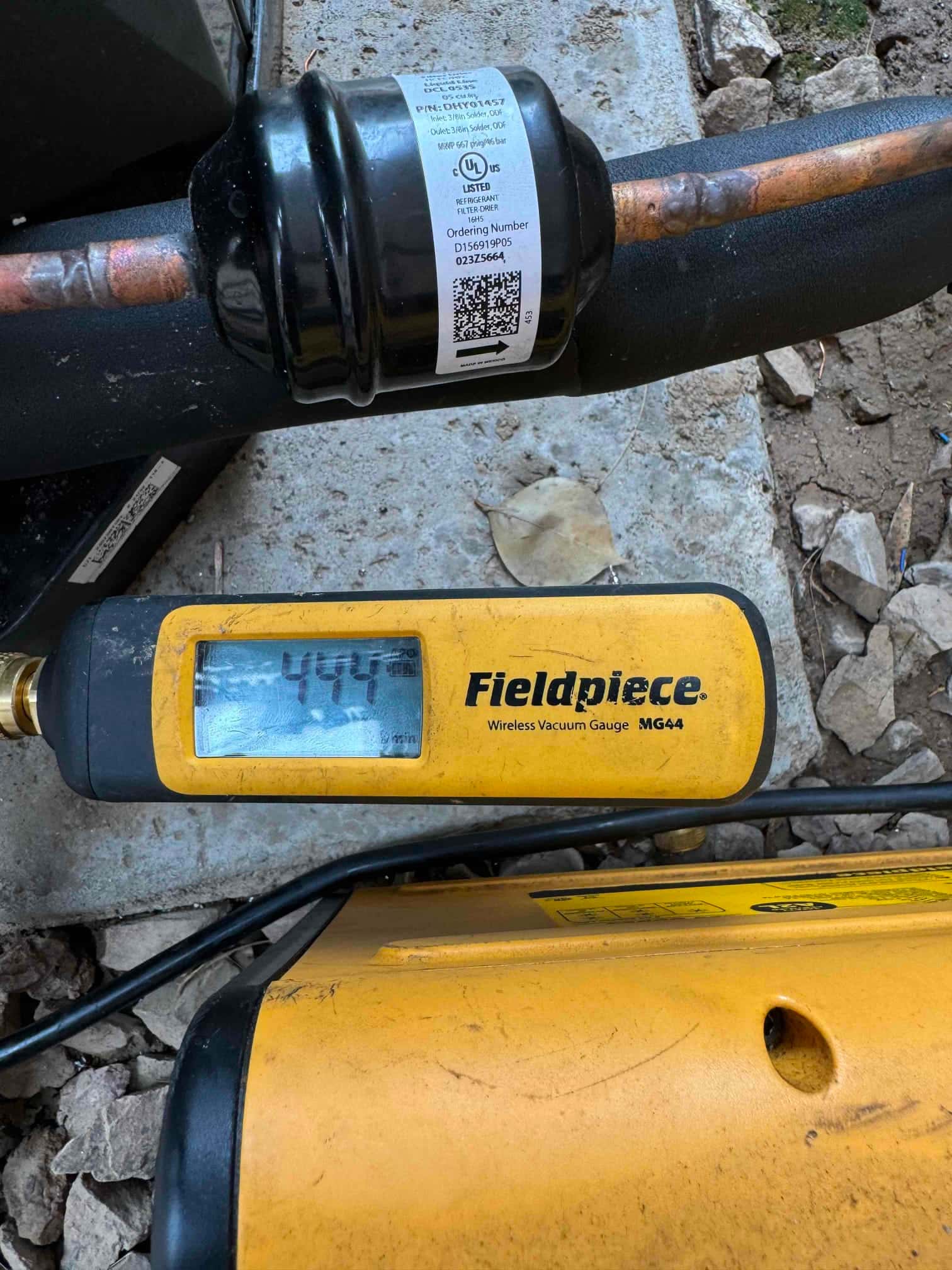 Wireless micron gauge reads 444 microns during evacuation beside the refrigerant line and inline filter-drier.