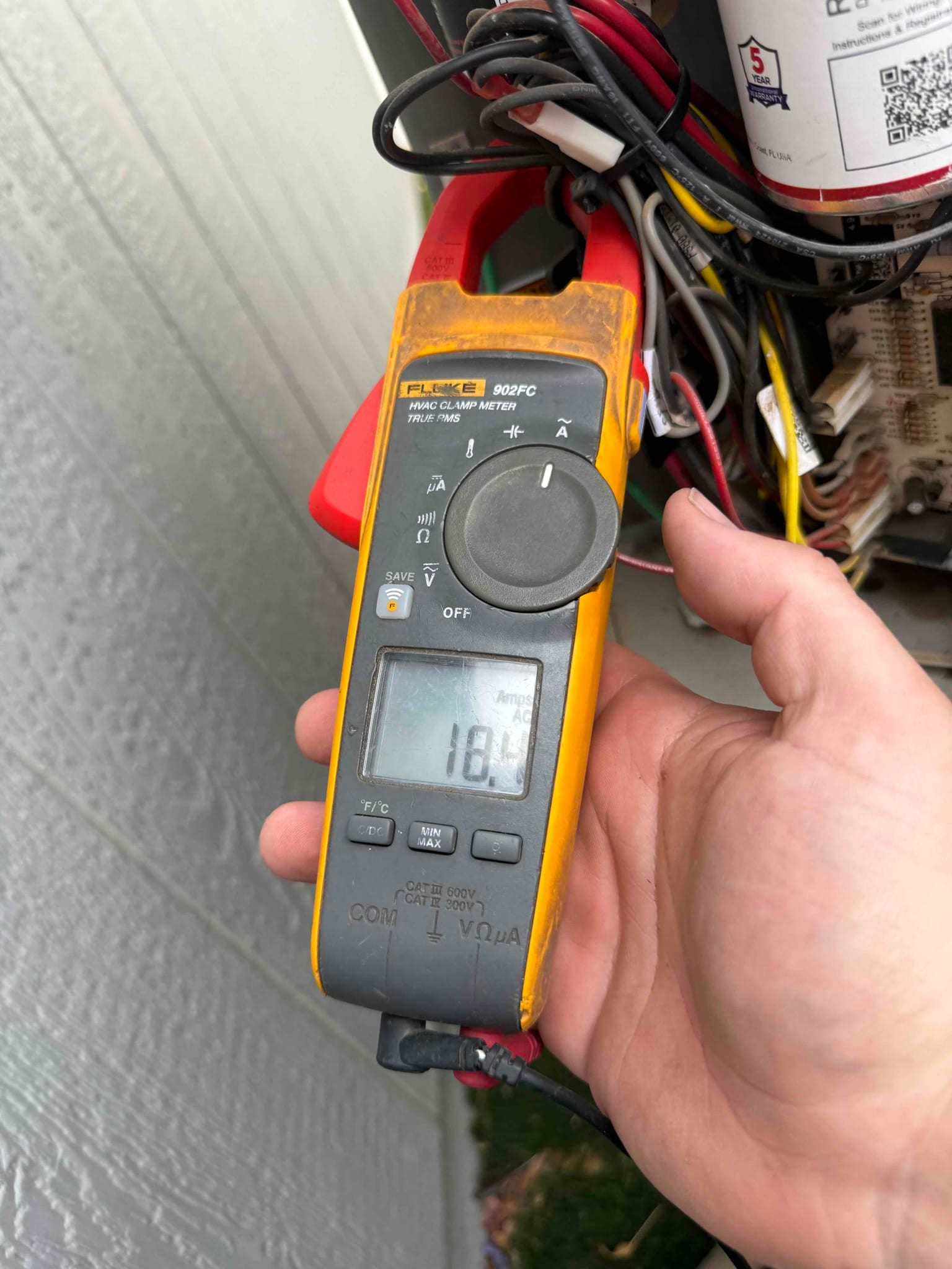 Clamp meter displays 18.4 A while clamped around an HVAC conductor near the control compartment.