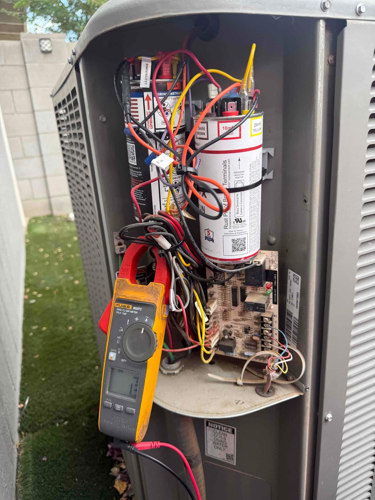 Digital multimeter measures 11.7 V at the control board inside the outdoor condenser with wiring and components exposed.