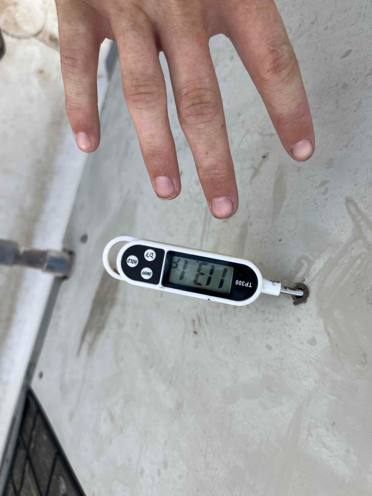 Digital thermometer measures 11.1 °C on a metal surface near HVAC equipment, showing the current surface temperature reading.