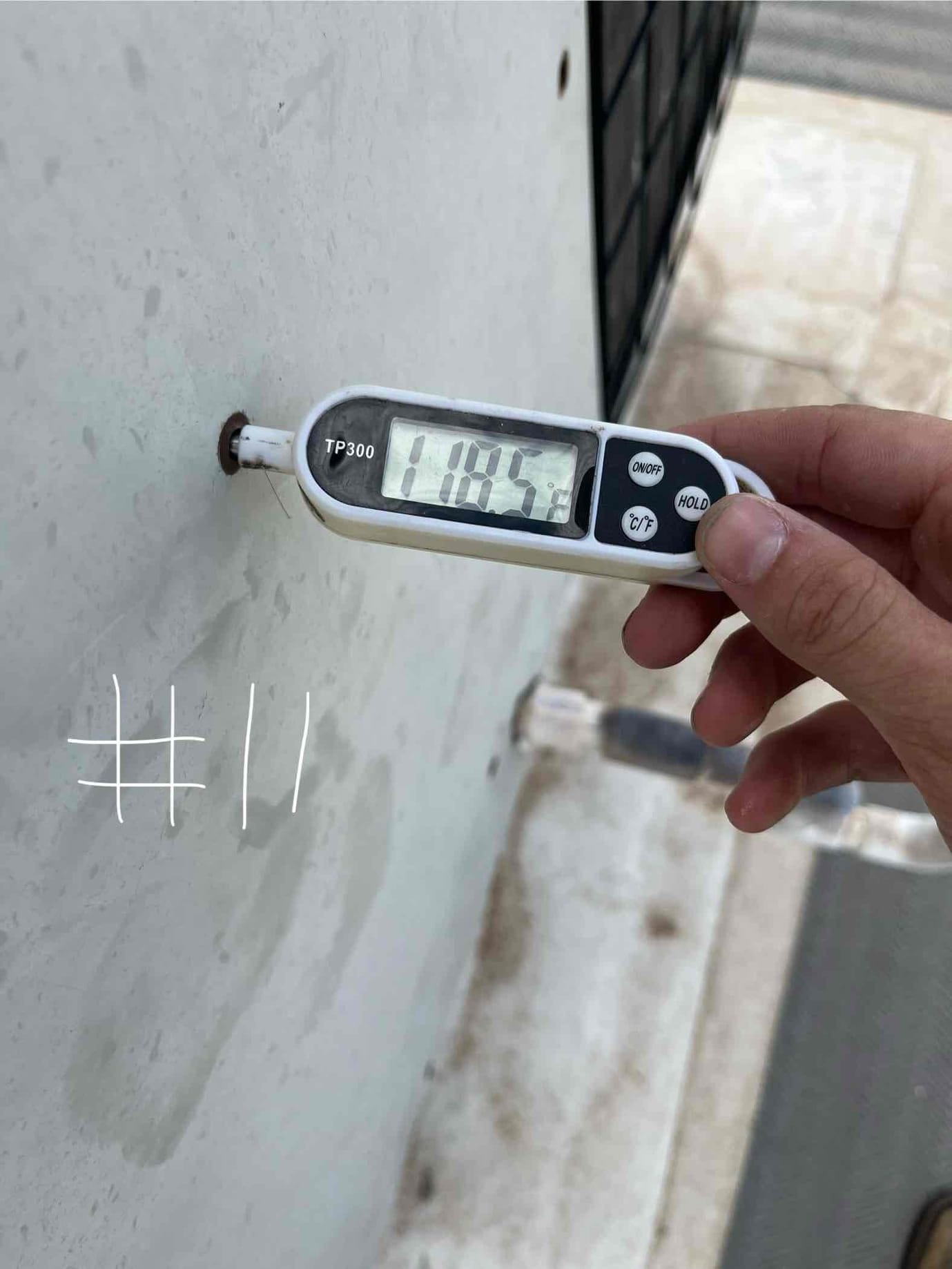 Digital thermometer shows 118.5 °F surface temperature on the outdoor unit’s metal panel near the condenser.